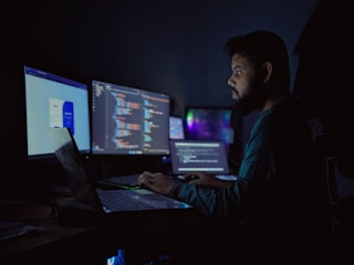 A man sitting in front of three computer monitors
