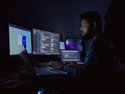 A man sitting in front of three computer monitors