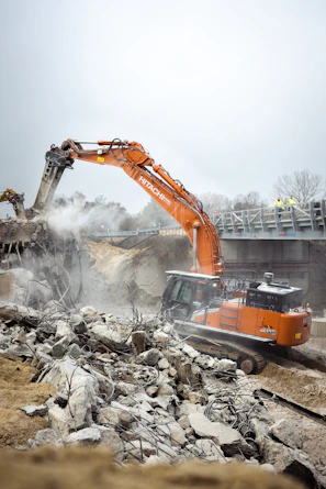 A large orange excavator digging through a pile of rubble