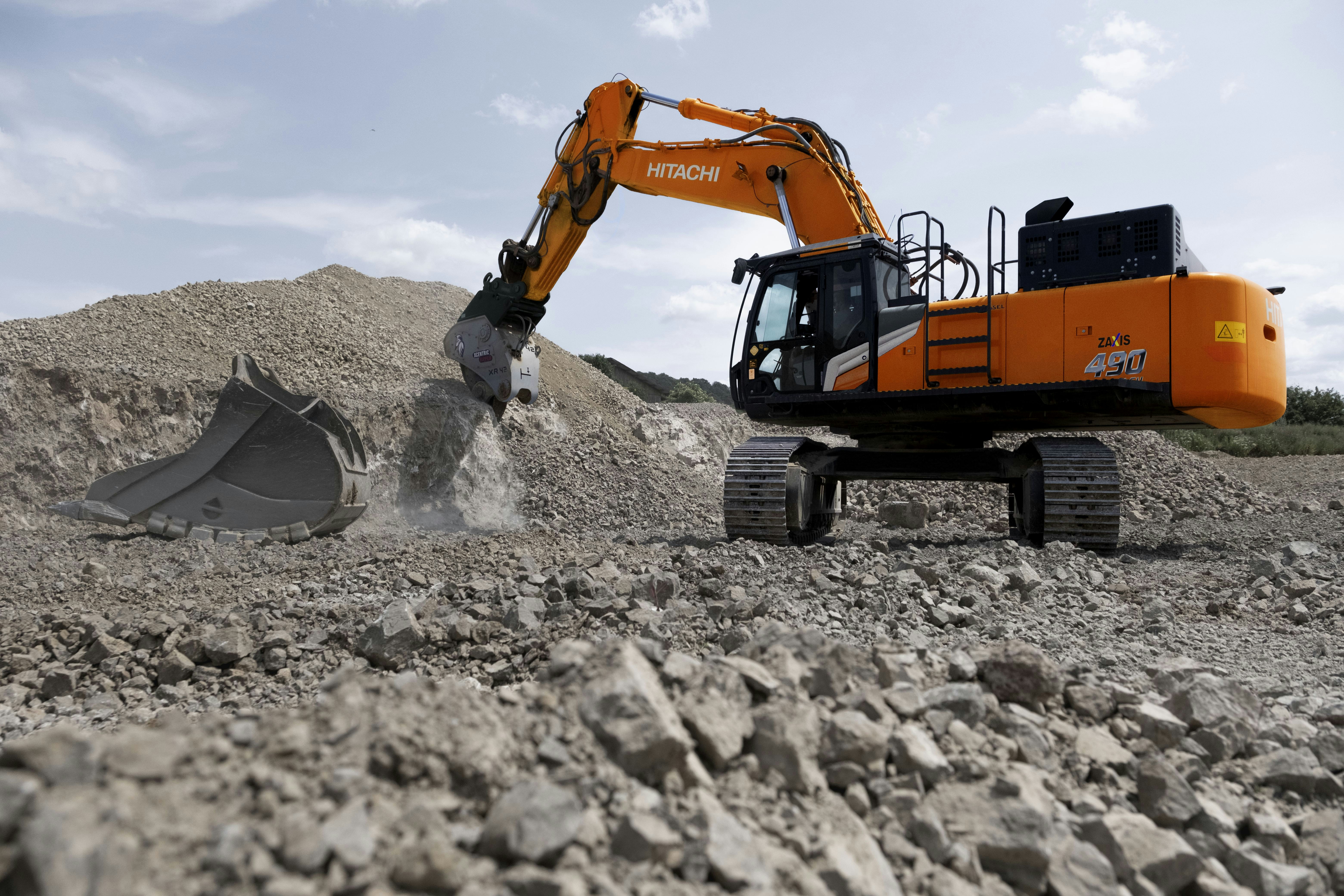 An orange excavator digging through a pile of rocks