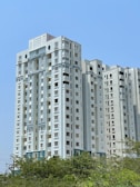 A tall white building sitting next to a lush green forest