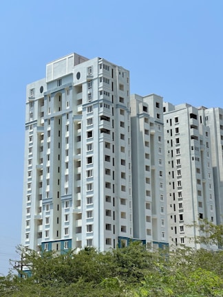 A tall white building sitting next to a lush green forest