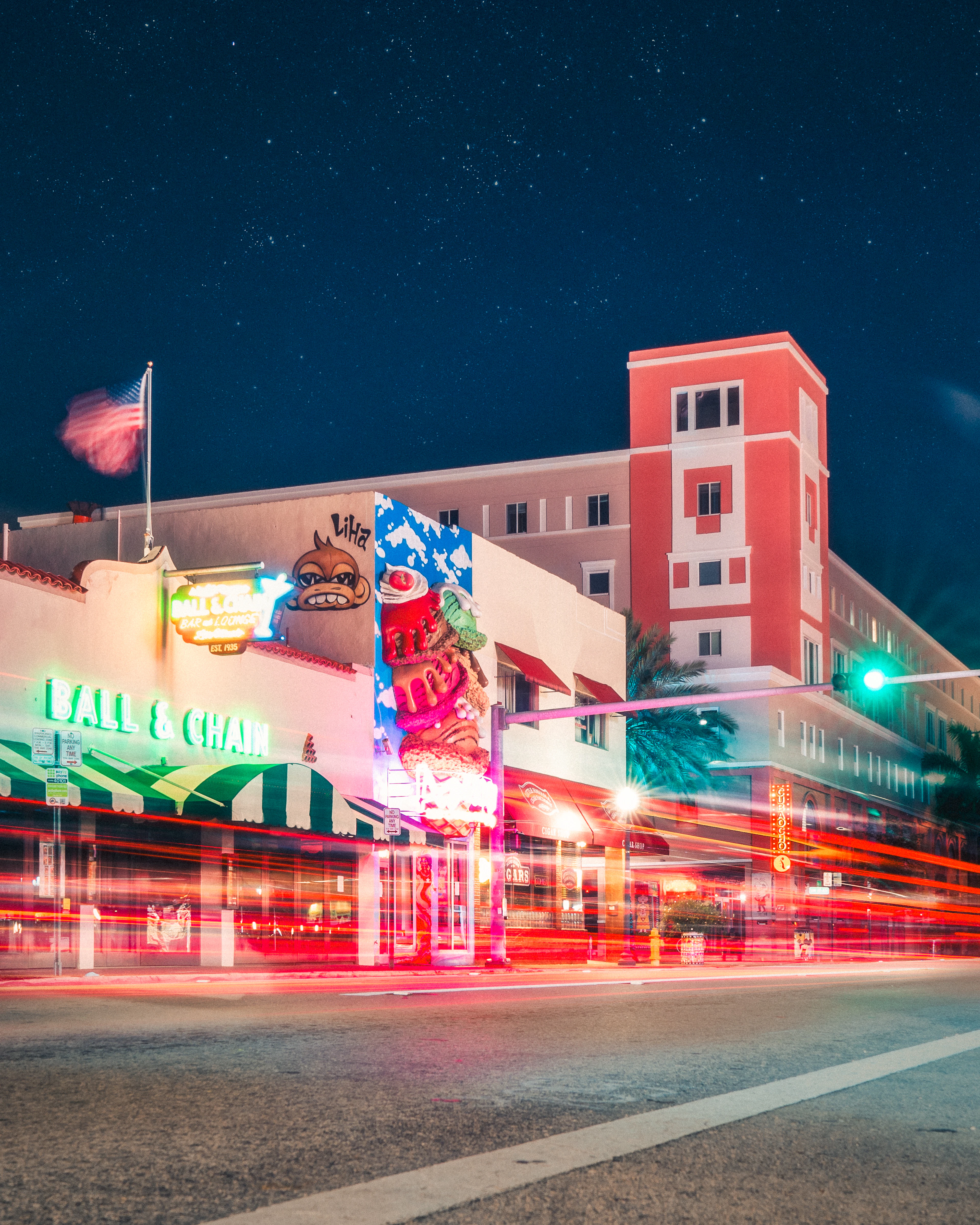 The neon frontage of the Ball & Chain club on Calle Ocho in Little Havana at night, its green sign and striped awnings glowing beneath a star-flecked sky as traffic streaks past in long red trails.