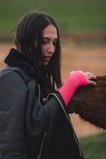 A woman in a black jacket petting a brown horse