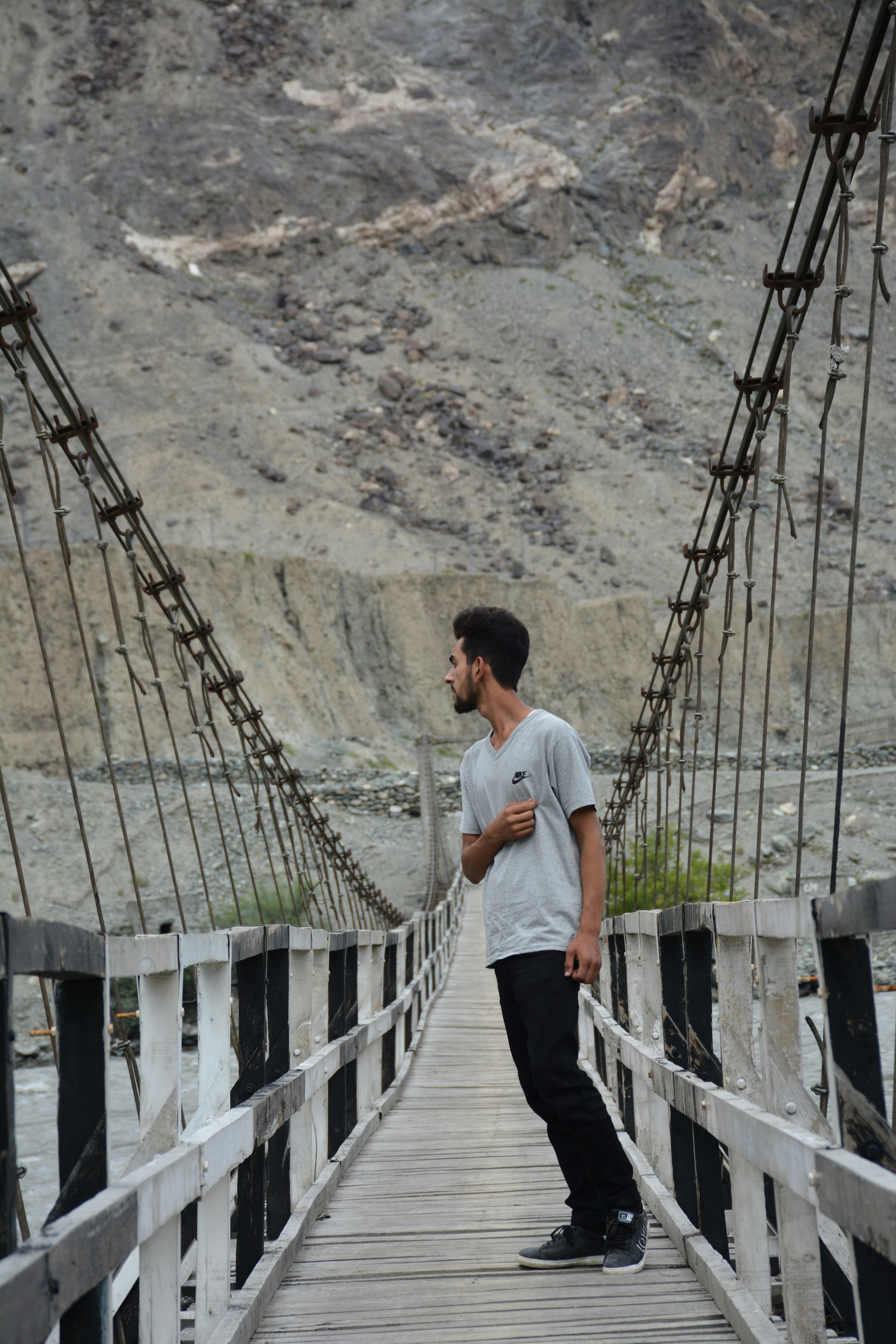 A man standing on a wooden bridge with mountains in the background
