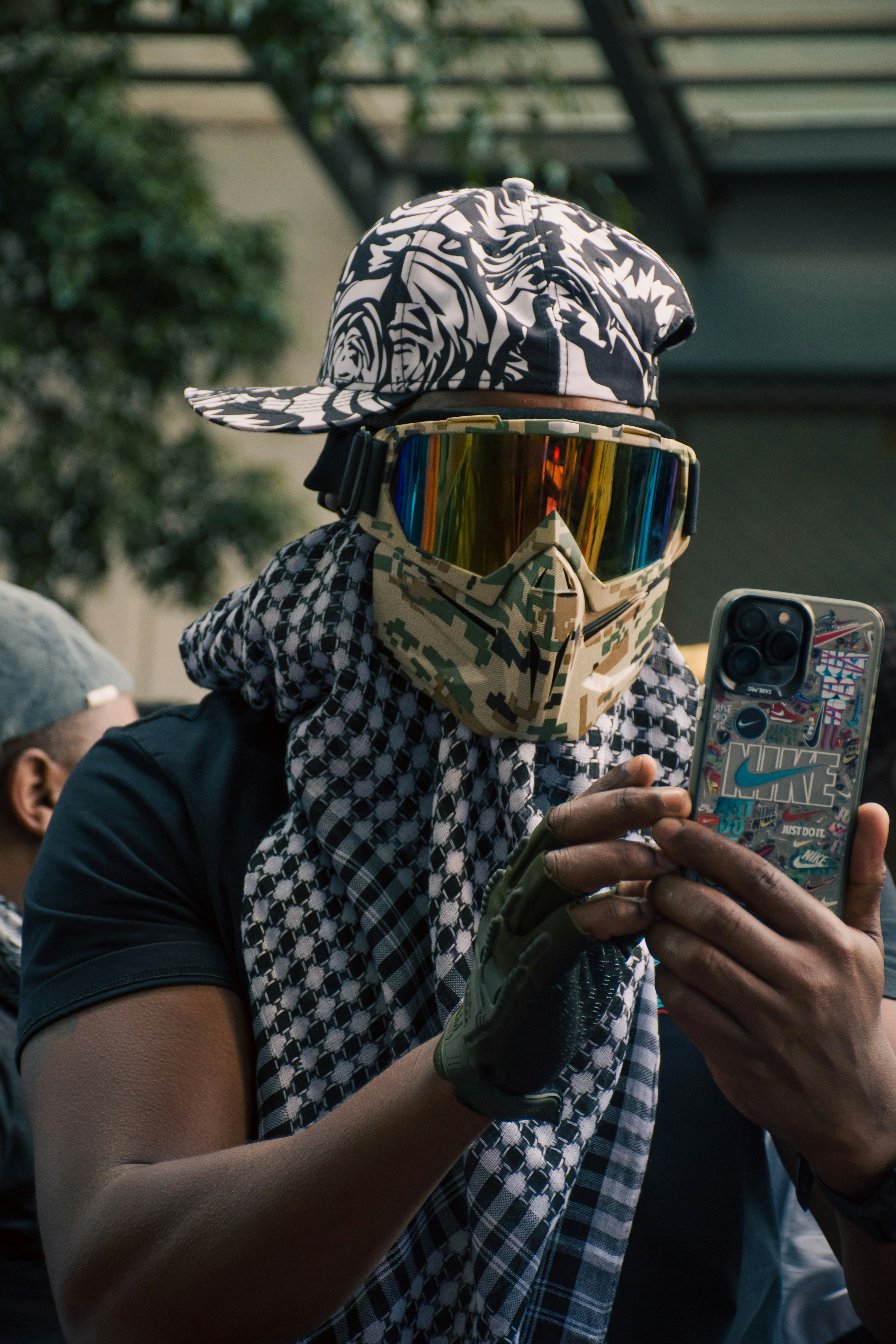 A man wearing a bandana and goggles taking a picture with his cell phone