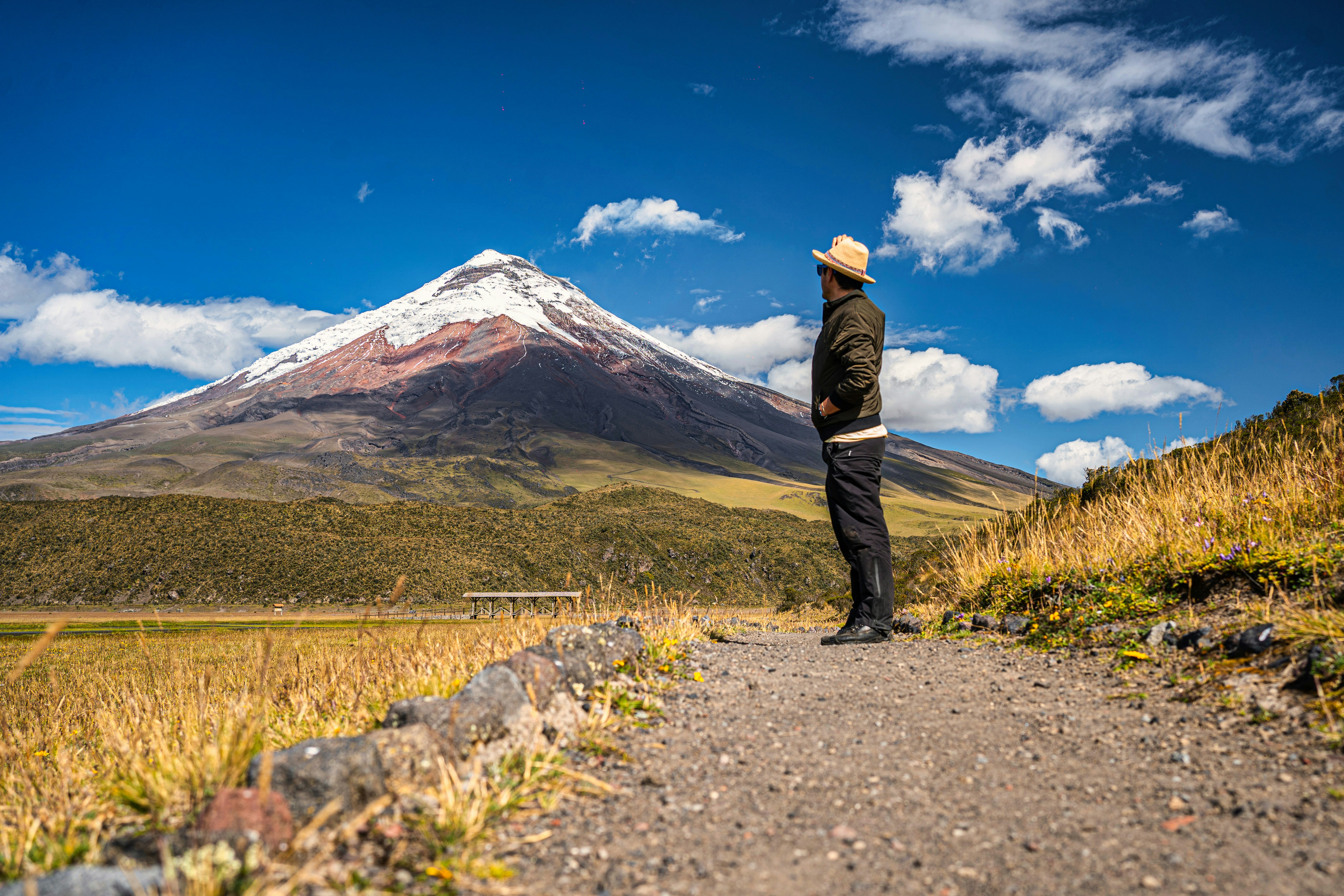 A man standing on a dirt road in front of a mountain, 