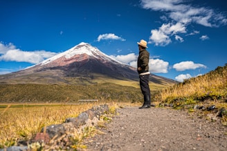 A man standing on a dirt road in front of a mountain