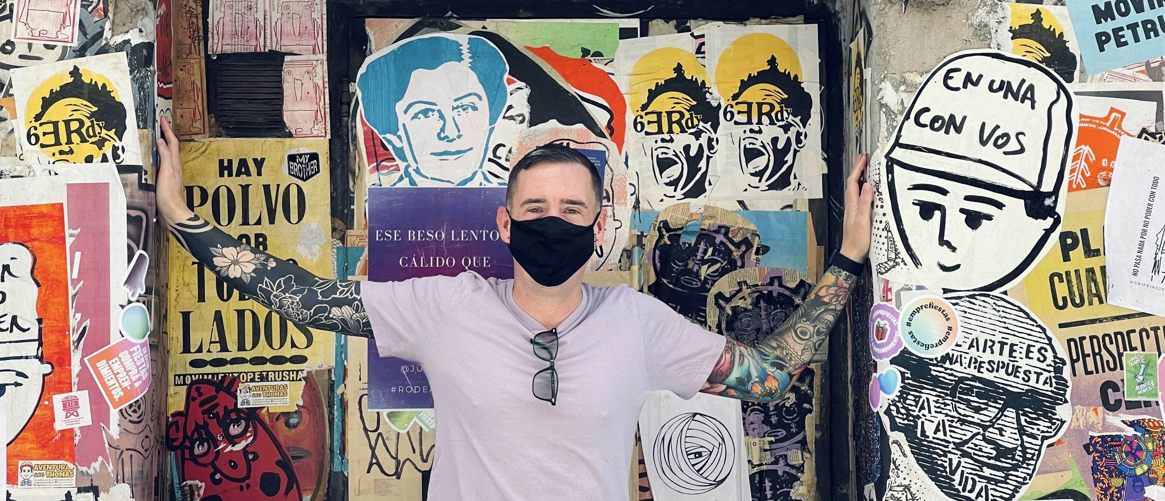 Un uomo che indossa una maschera facciale in piedi davanti a un muro coperto di poster