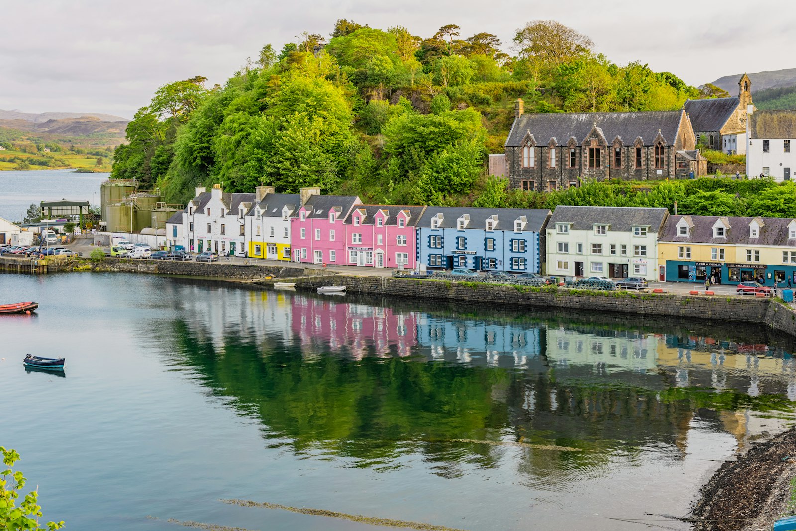 Pastel-coloured harbourfront houses reflected in calm water with small boats moored along the quay
