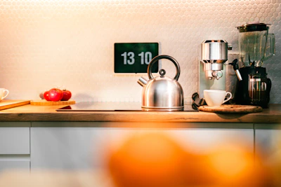 A kitchen counter with a tea kettle, oranges, and other kitchen items