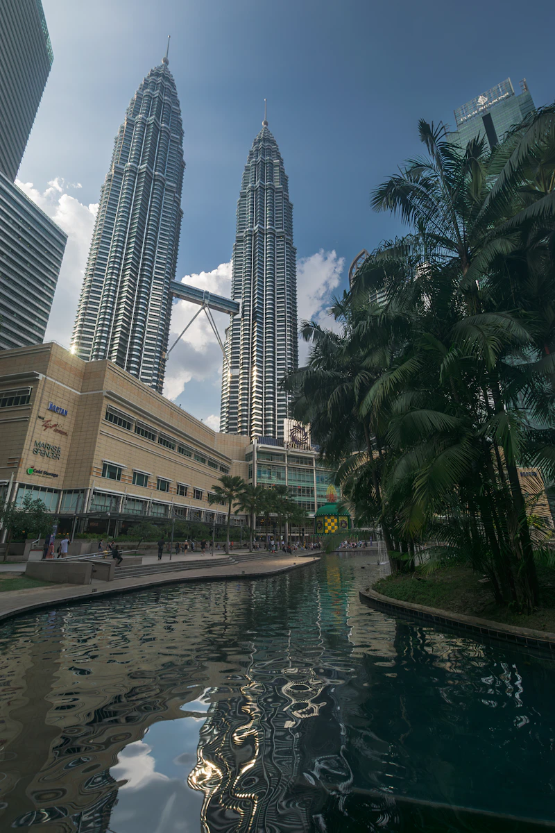 Petronas Twin Towers behind palm trees and a water channel in KLCC Park