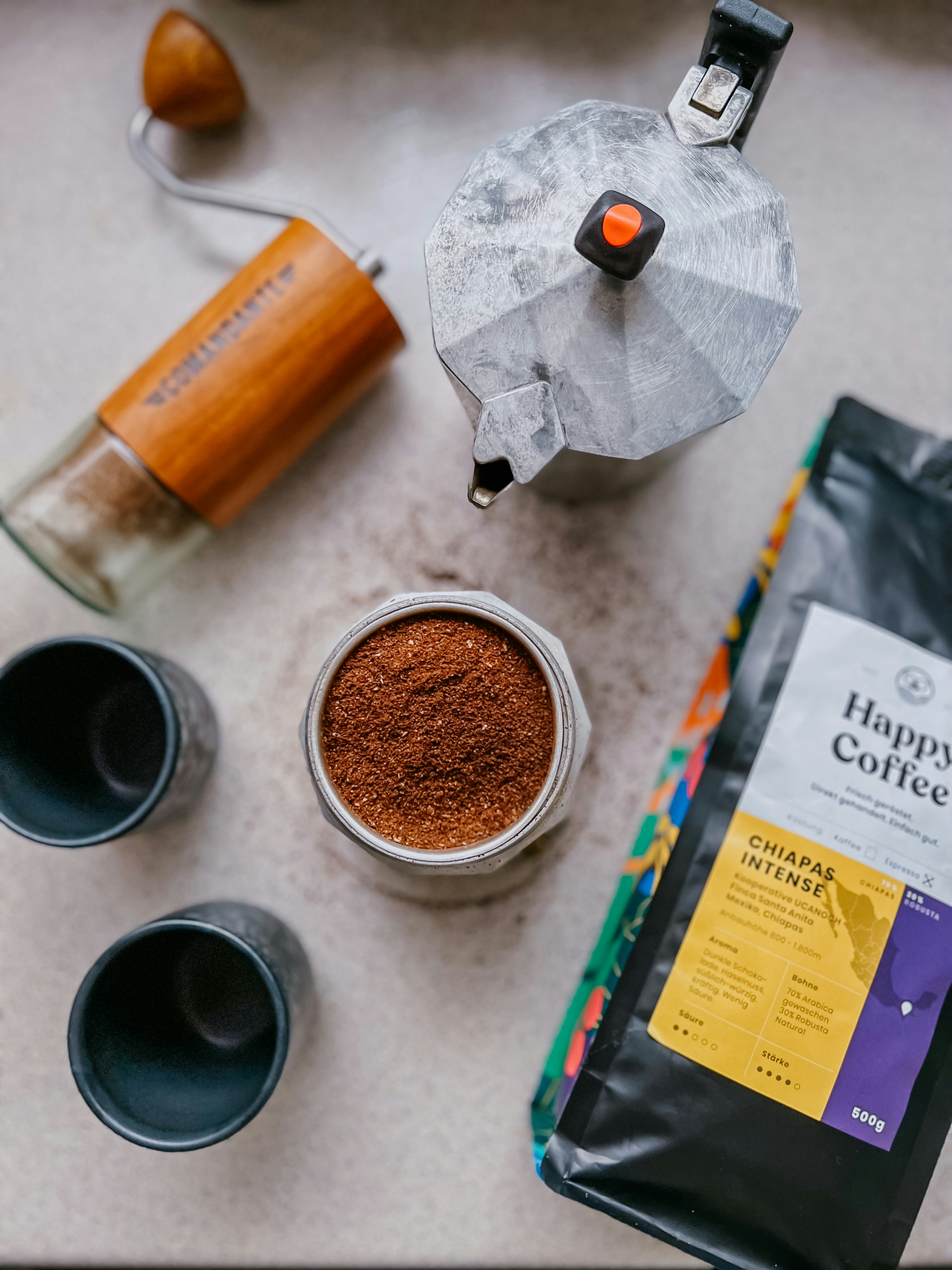 A coffee grinder, a cup of coffee, a bag of coffee beans,