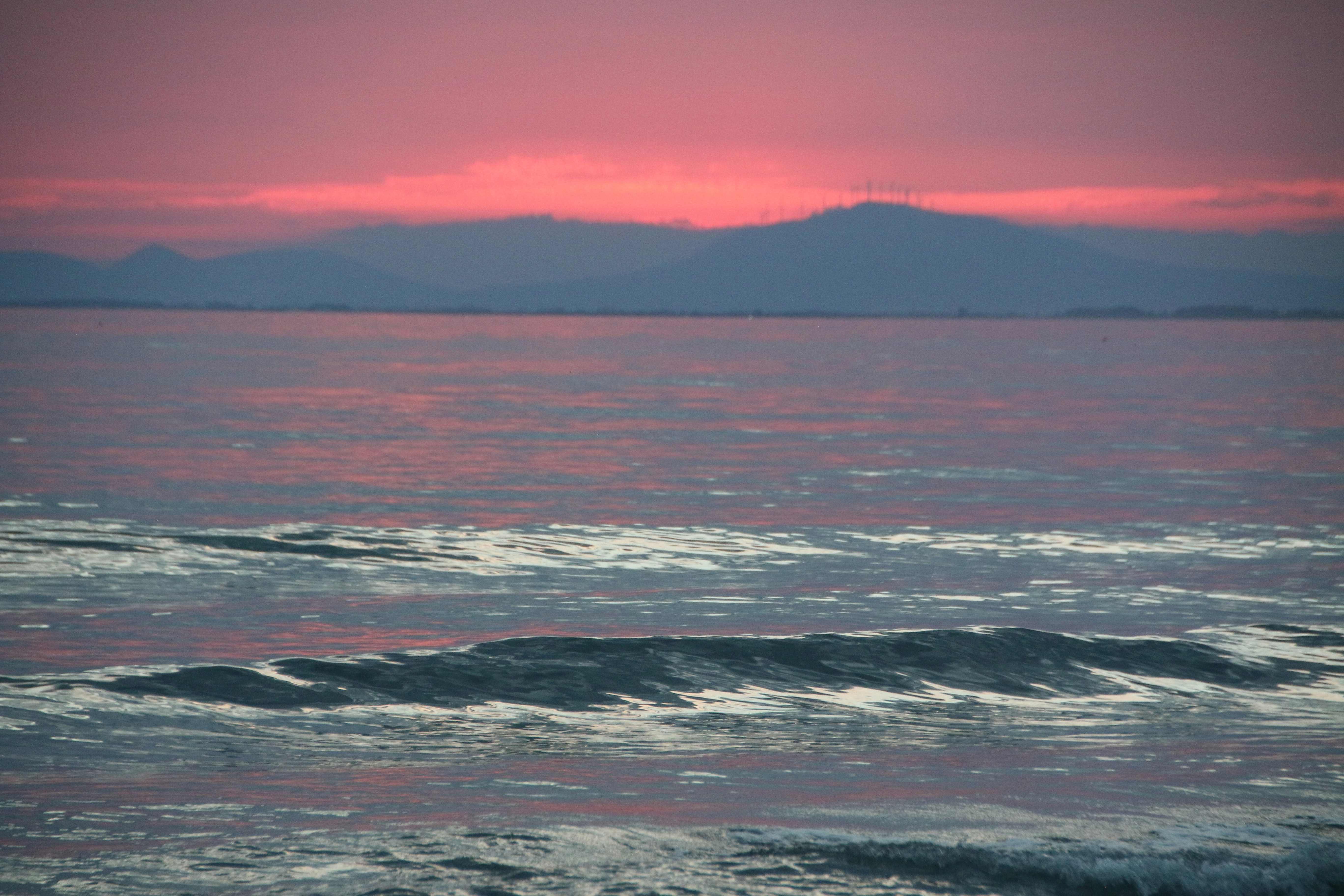 The sun is setting over the ocean with mountains in the distance