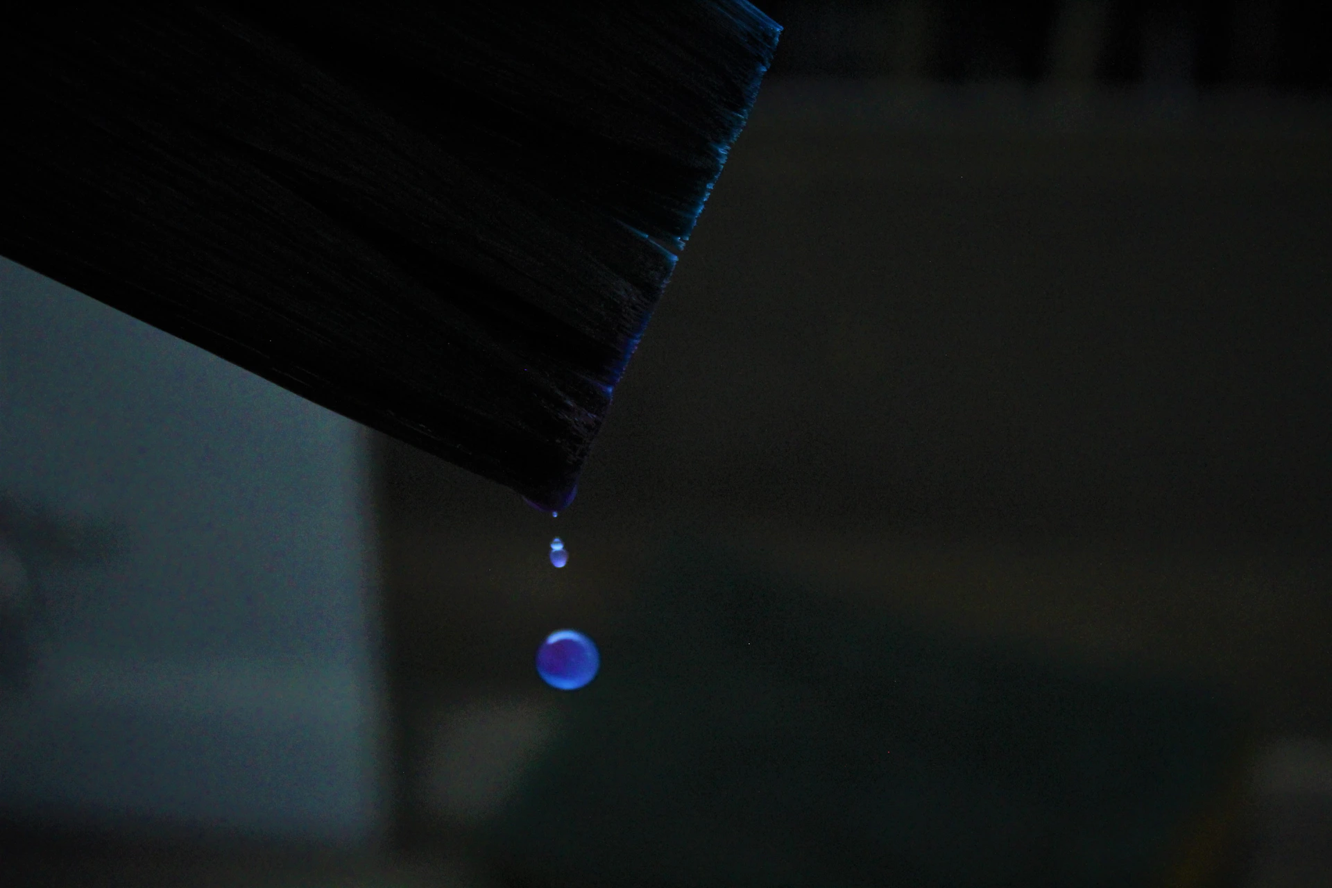 A drop of water hanging from a black umbrella