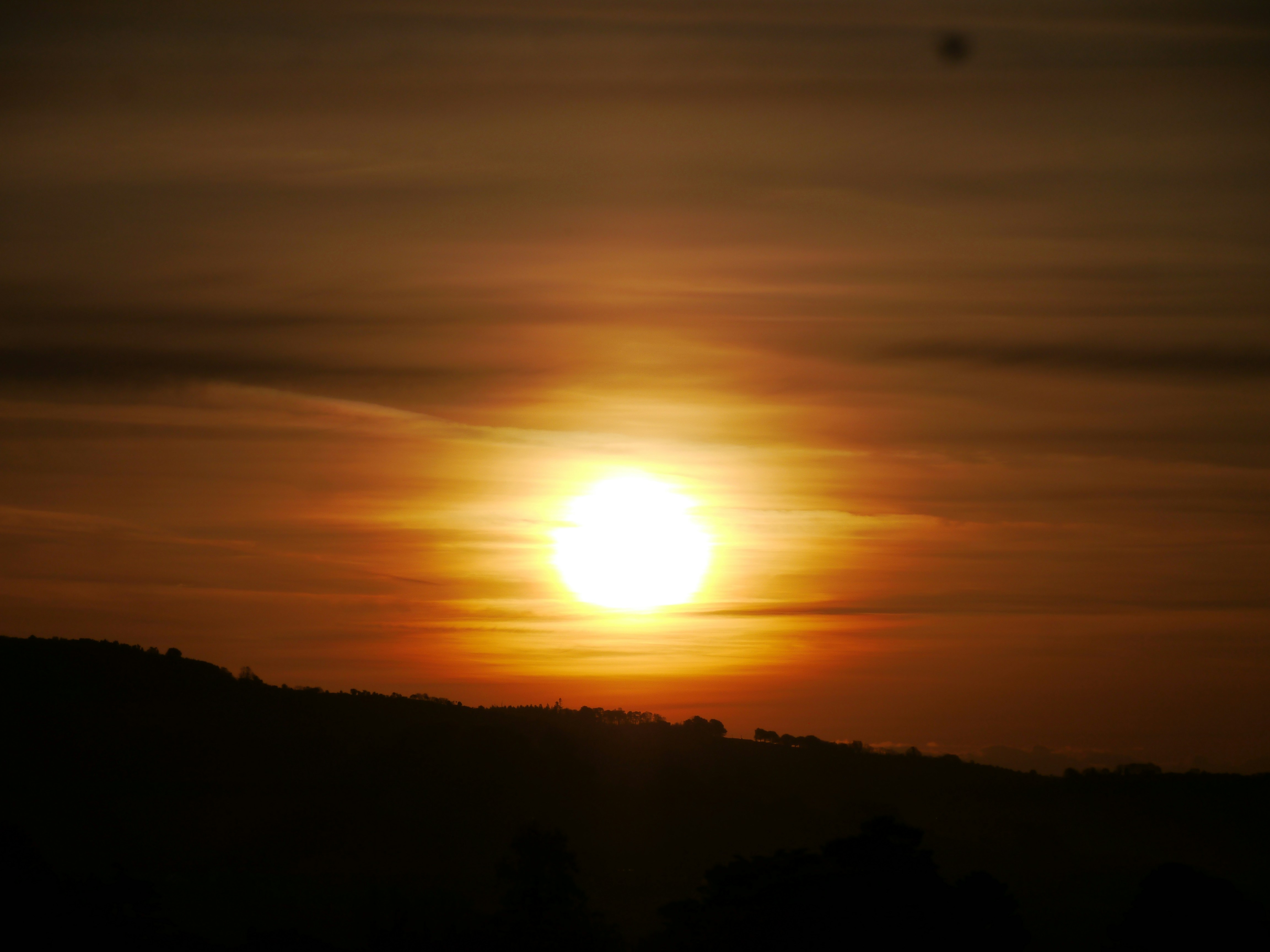 The sun is setting in the sky over a hill
