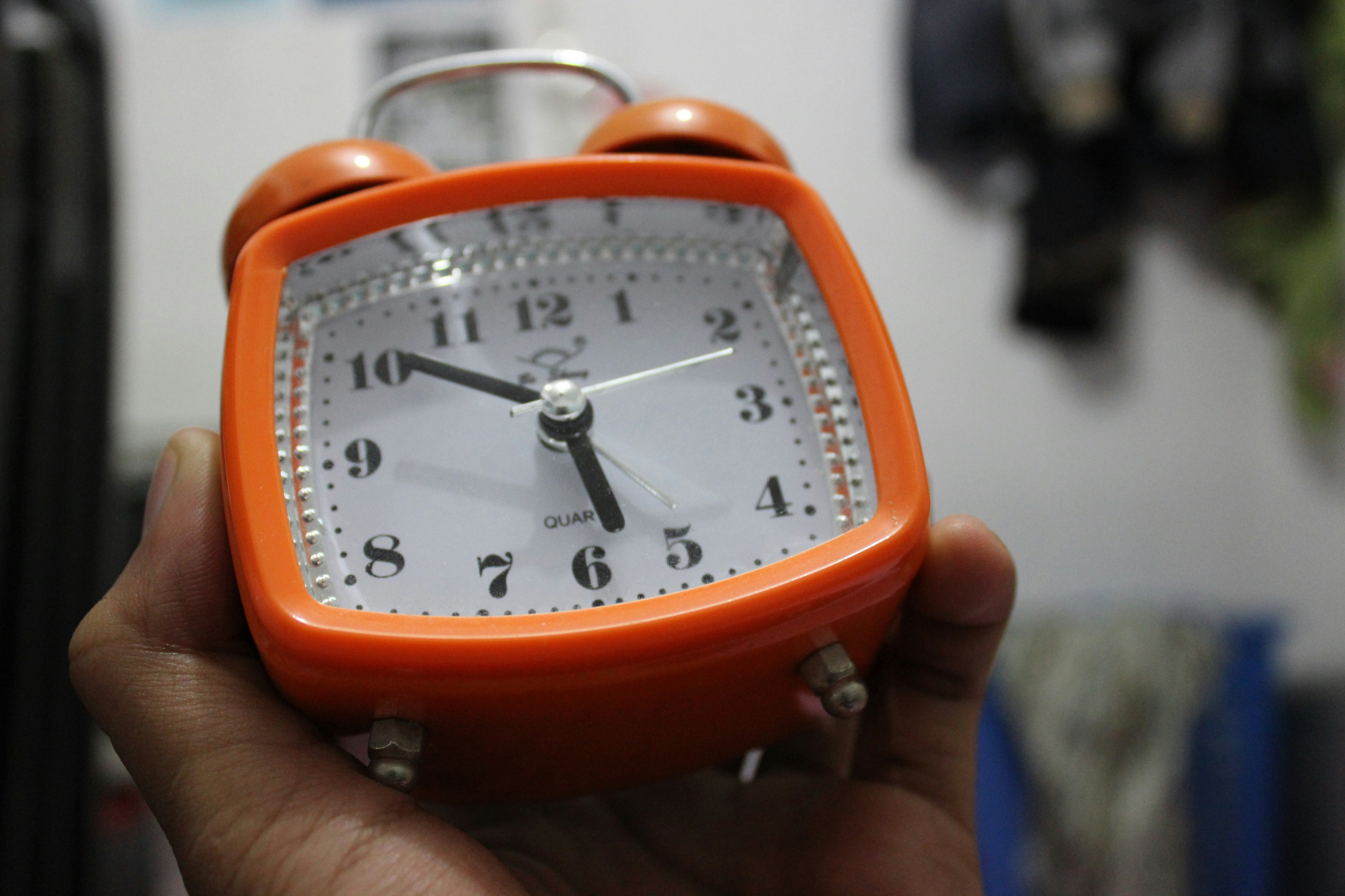A person holding a small orange clock in their hand