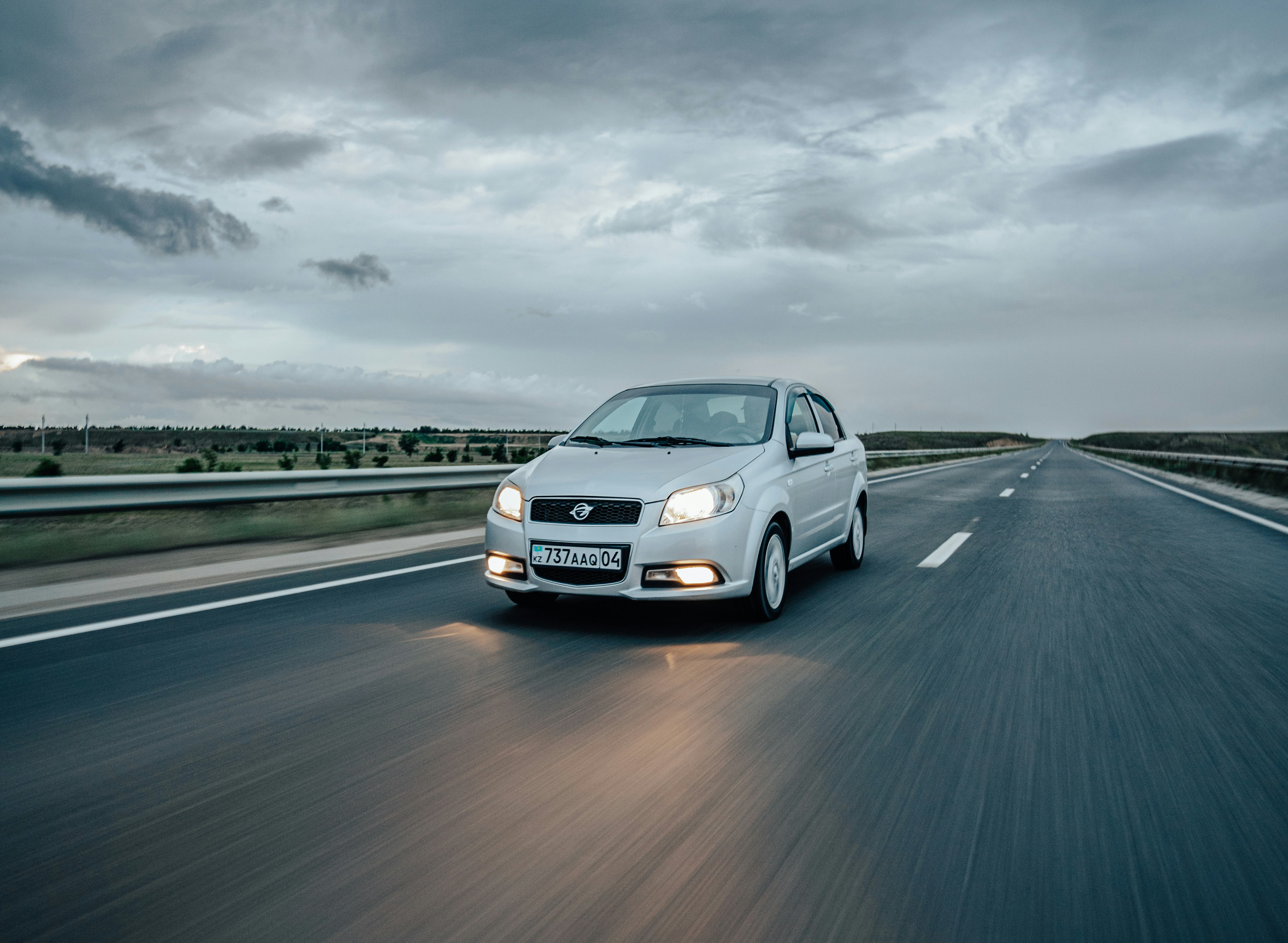 A white car driving down a highway under a cloudy sky