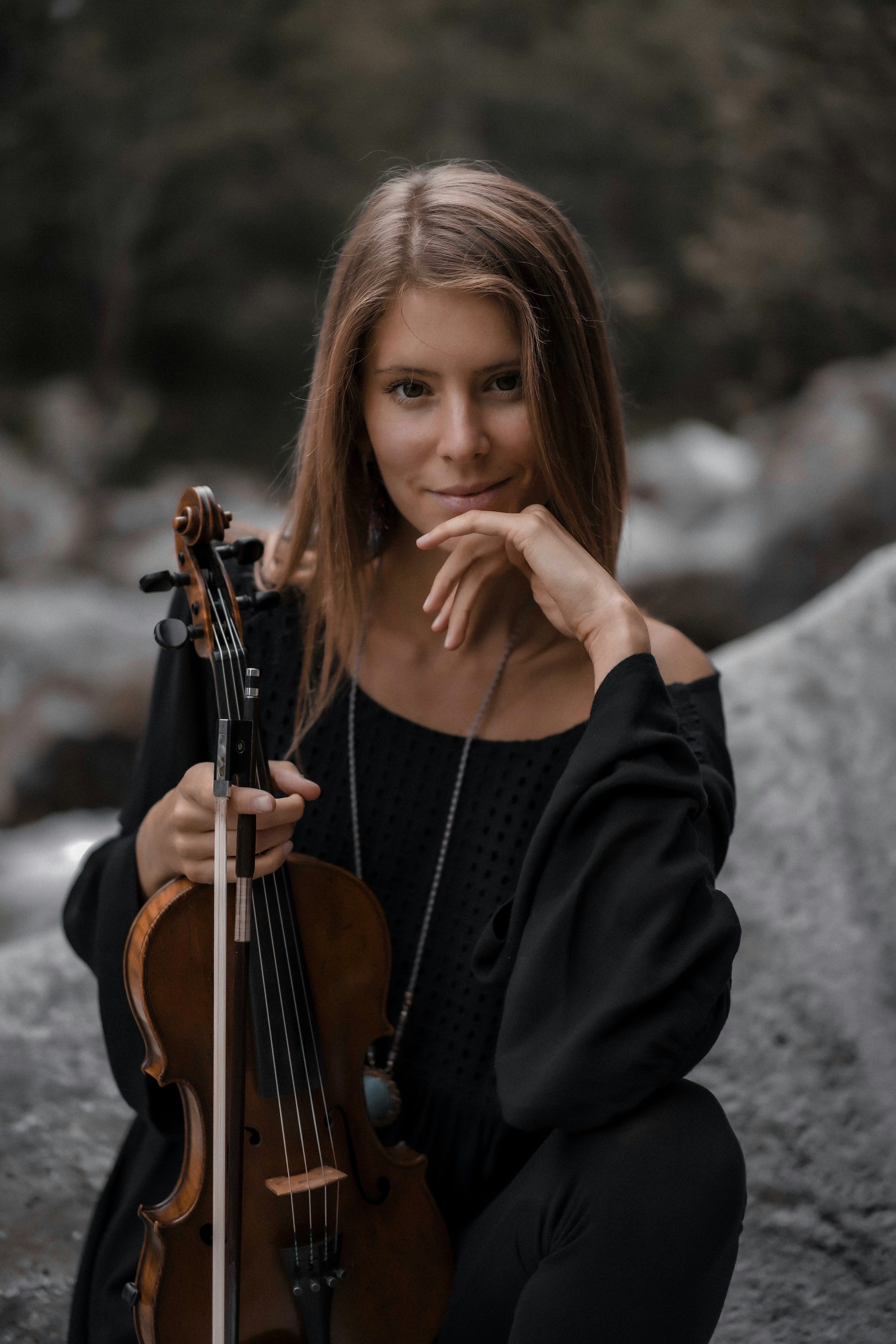 Eine Frau sitzt auf einem Felsen und hält eine Geige in der Hand