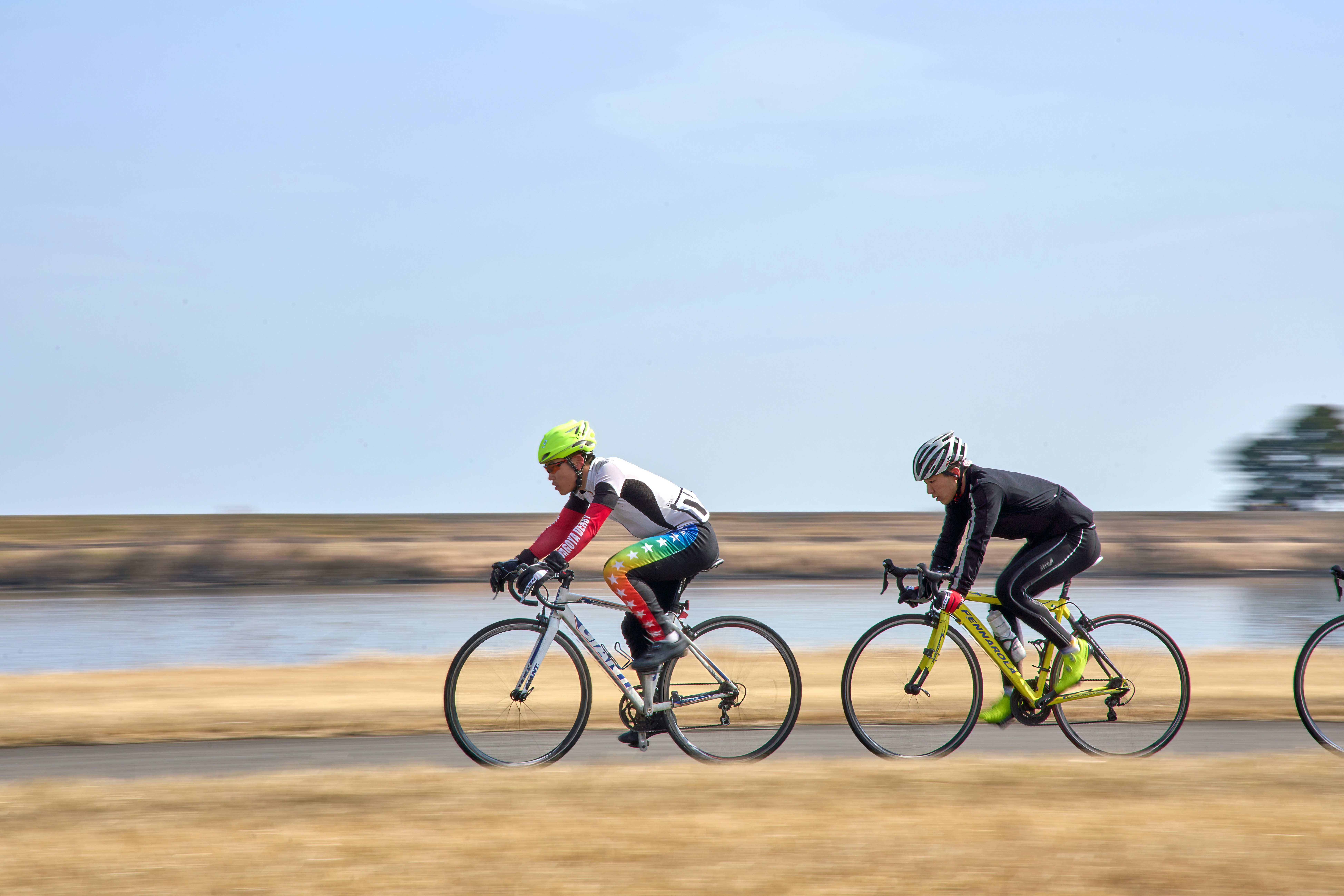 Three bicyclists riding down a road near a body of water