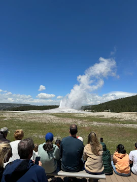 A group of people sitting on a bench watching a geyser