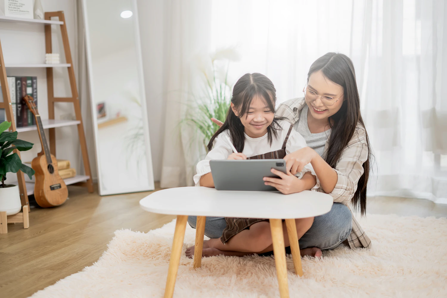 A mother and daughter sitting on the floor looking at a tablet together