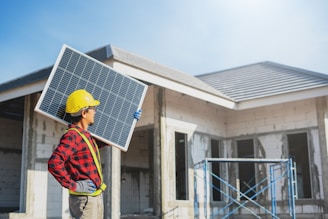 A man holding a solar panel in front of a house