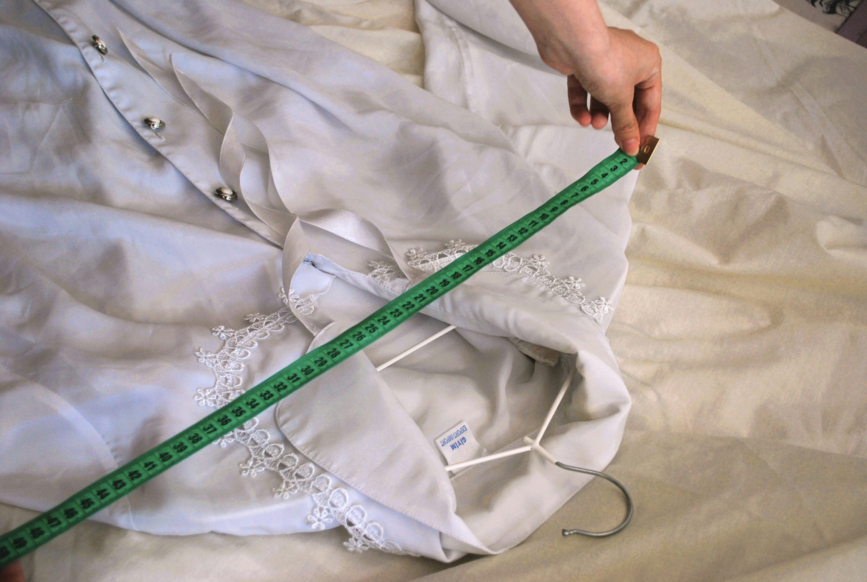 A person measuring a white shirt with a green measuring tape