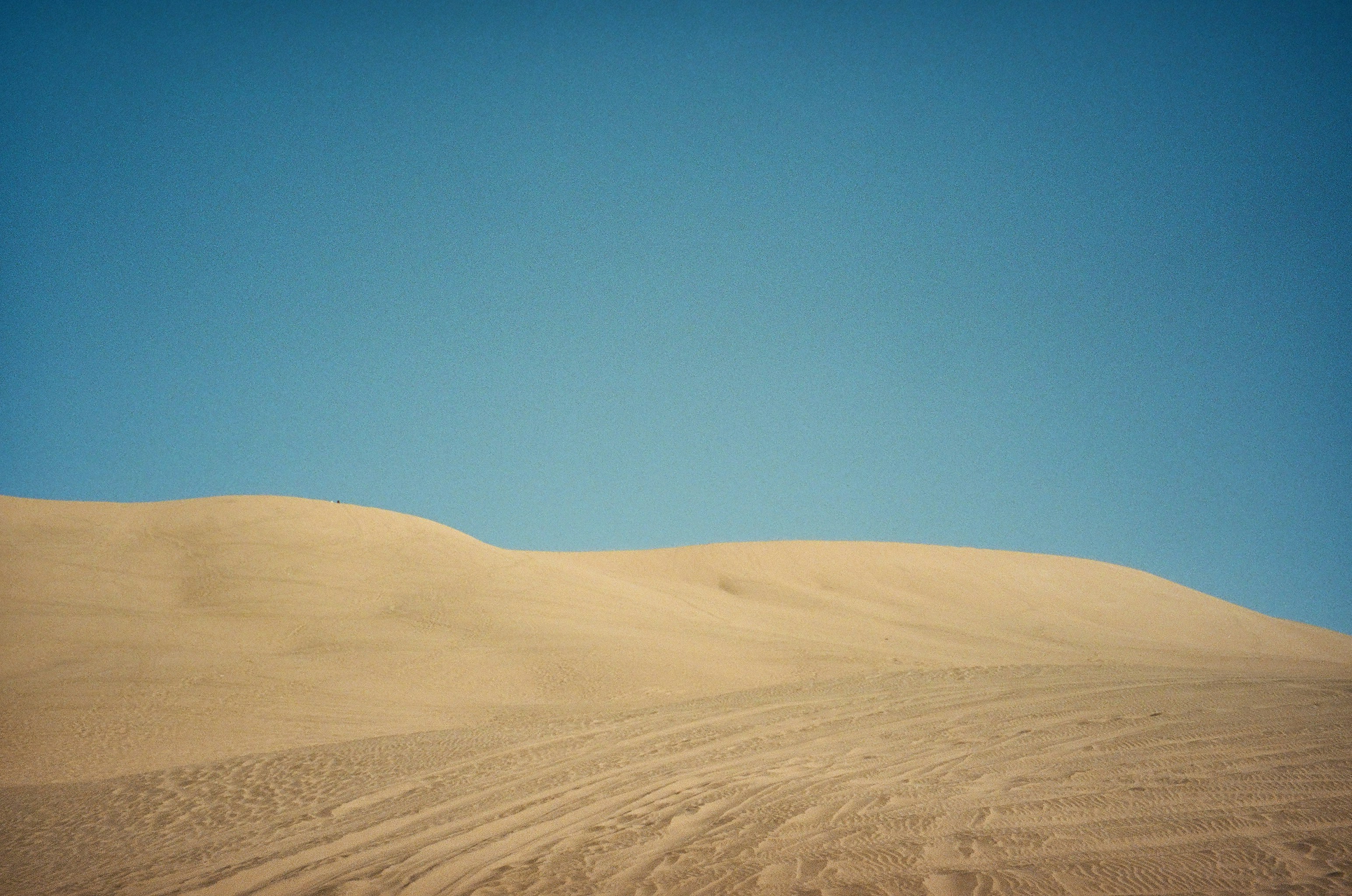 A large sand dune with a blue sky in the background