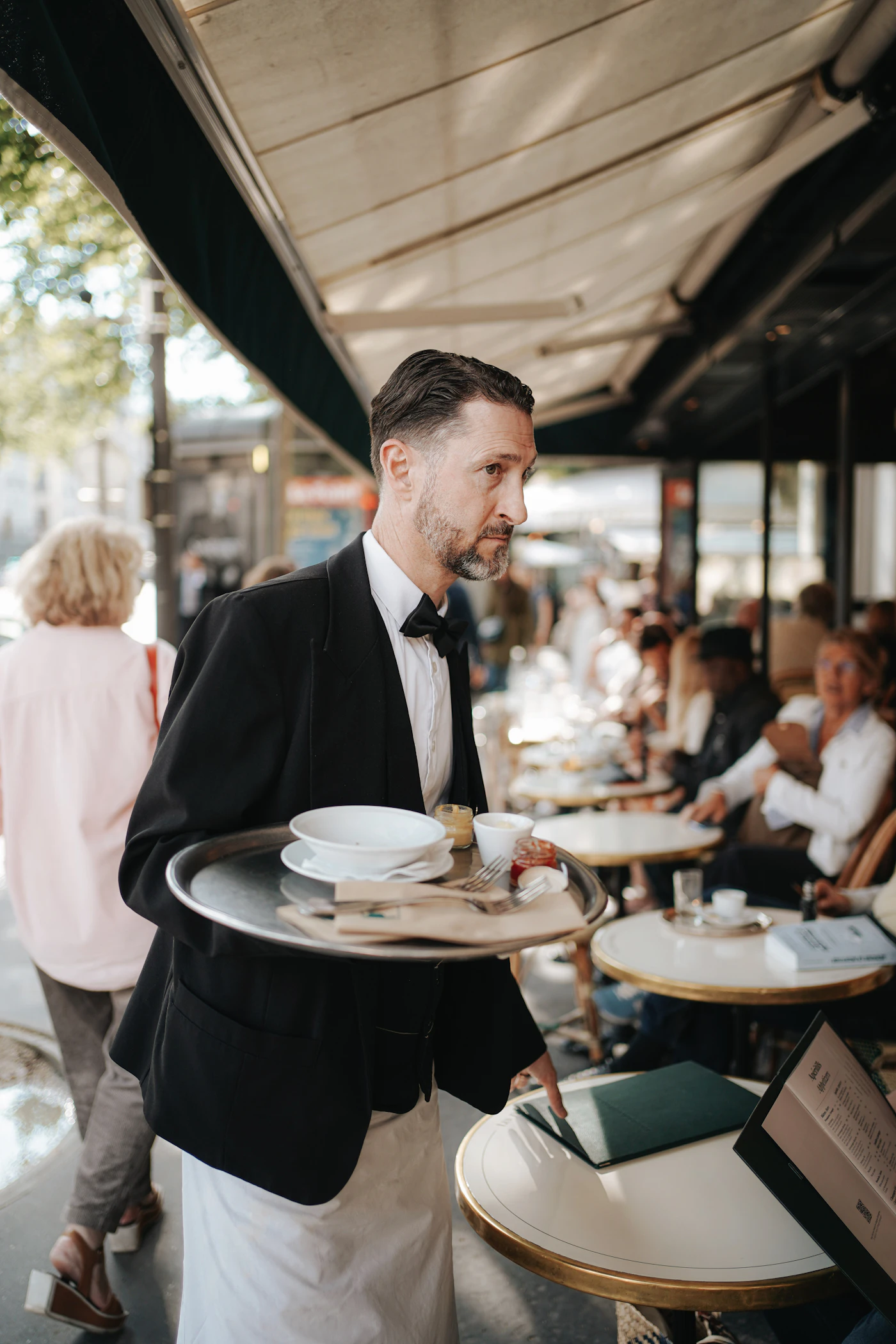 Servitör i väst och fluga som bär en bricka mellan borden på en restaurang