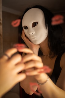 A woman wearing a white mask looking at her reflection in a mirror