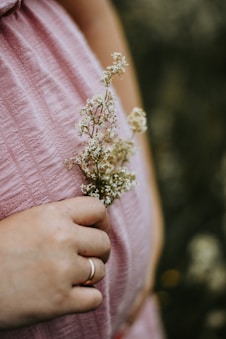 A pregnant woman in a pink dress holding a flower