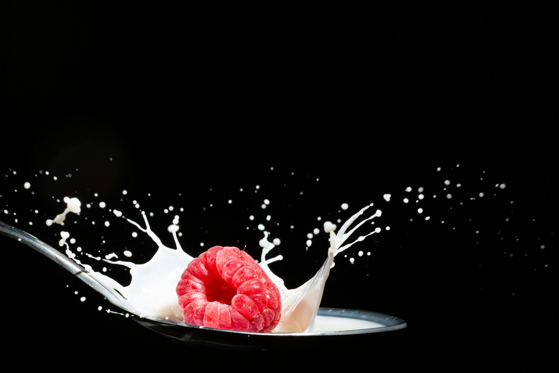 A raspberry splashing into a bowl of milk