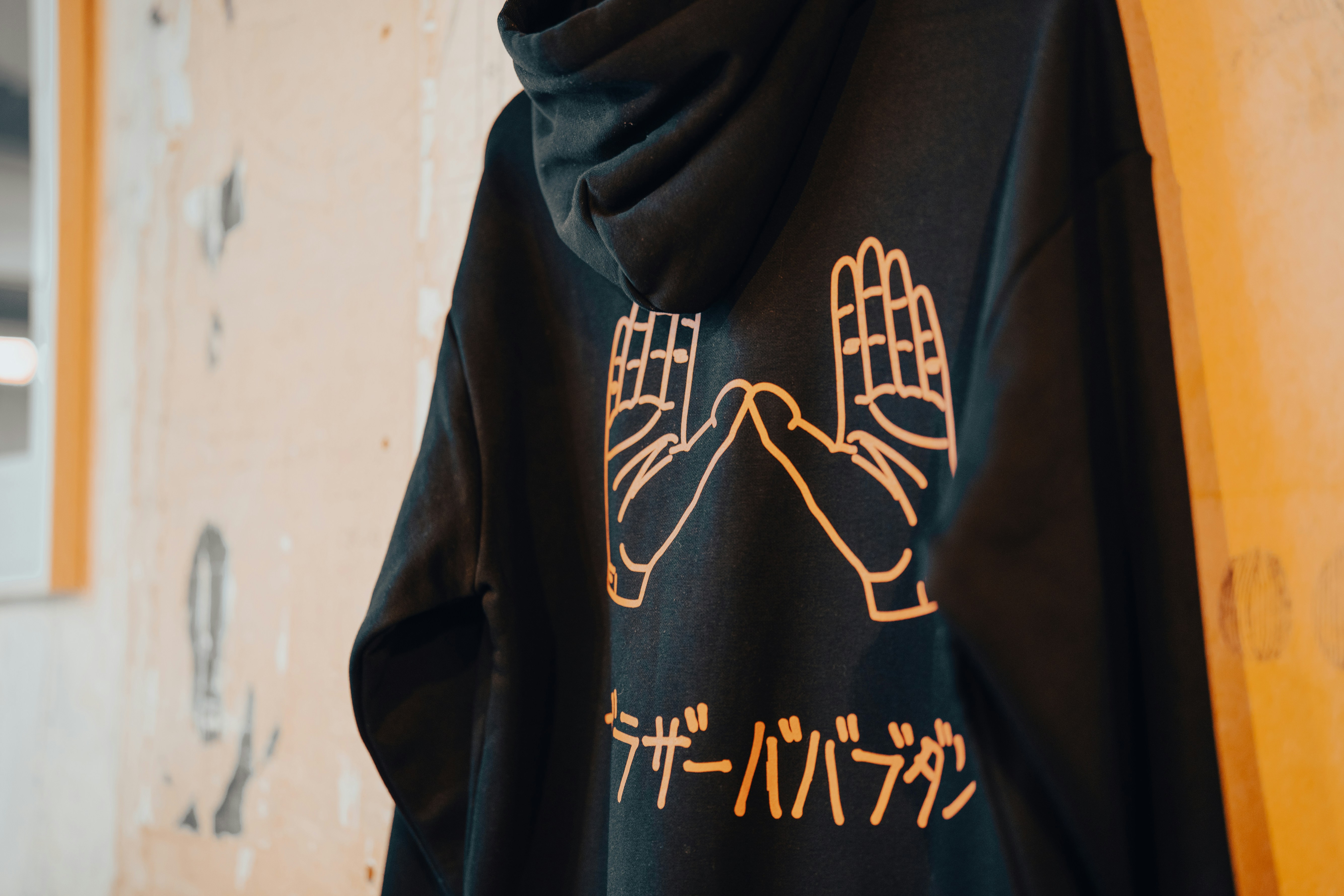 Black hoodie with an orange hand design hanging on a wall.