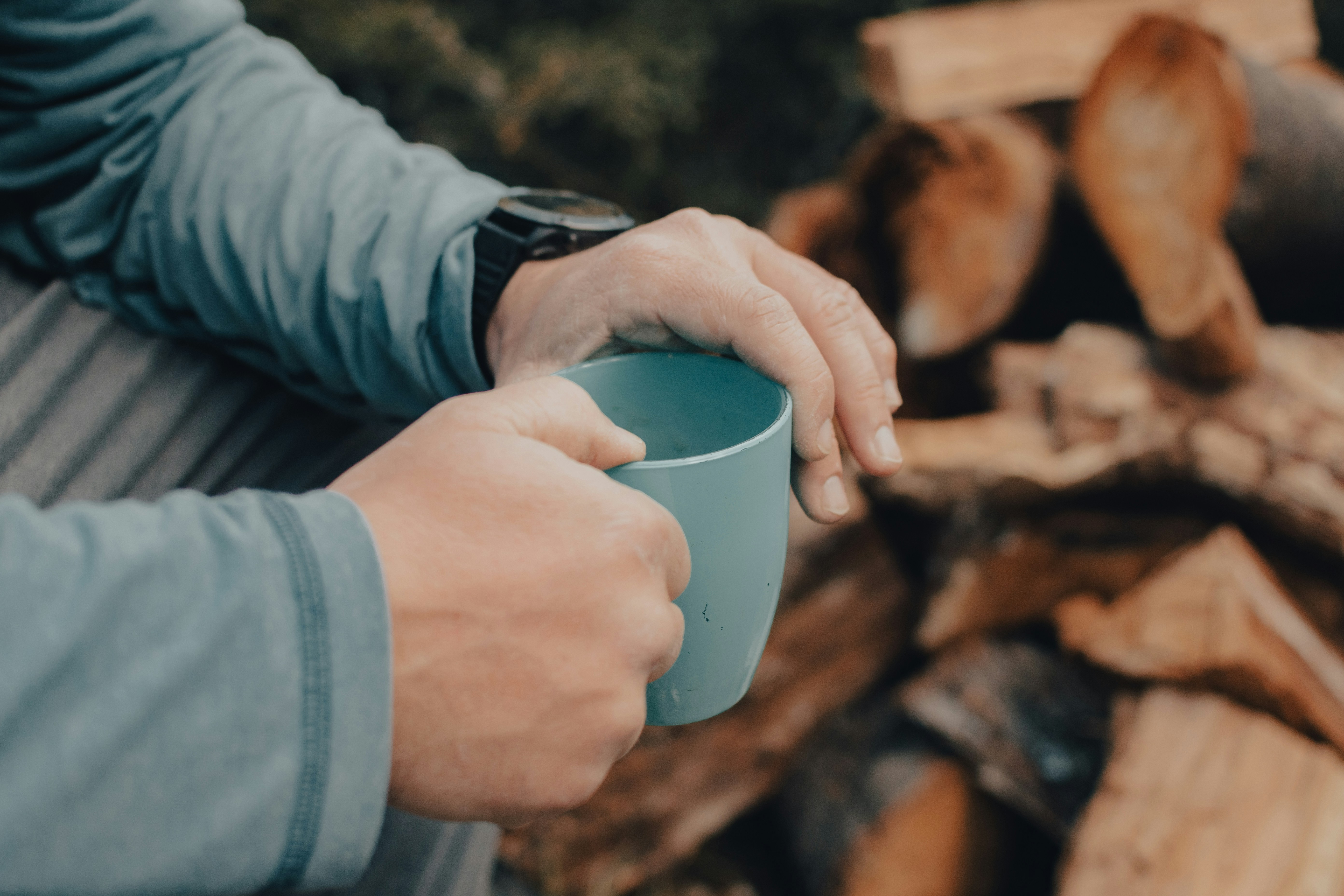 A person holding a cup in front of a pile of wood