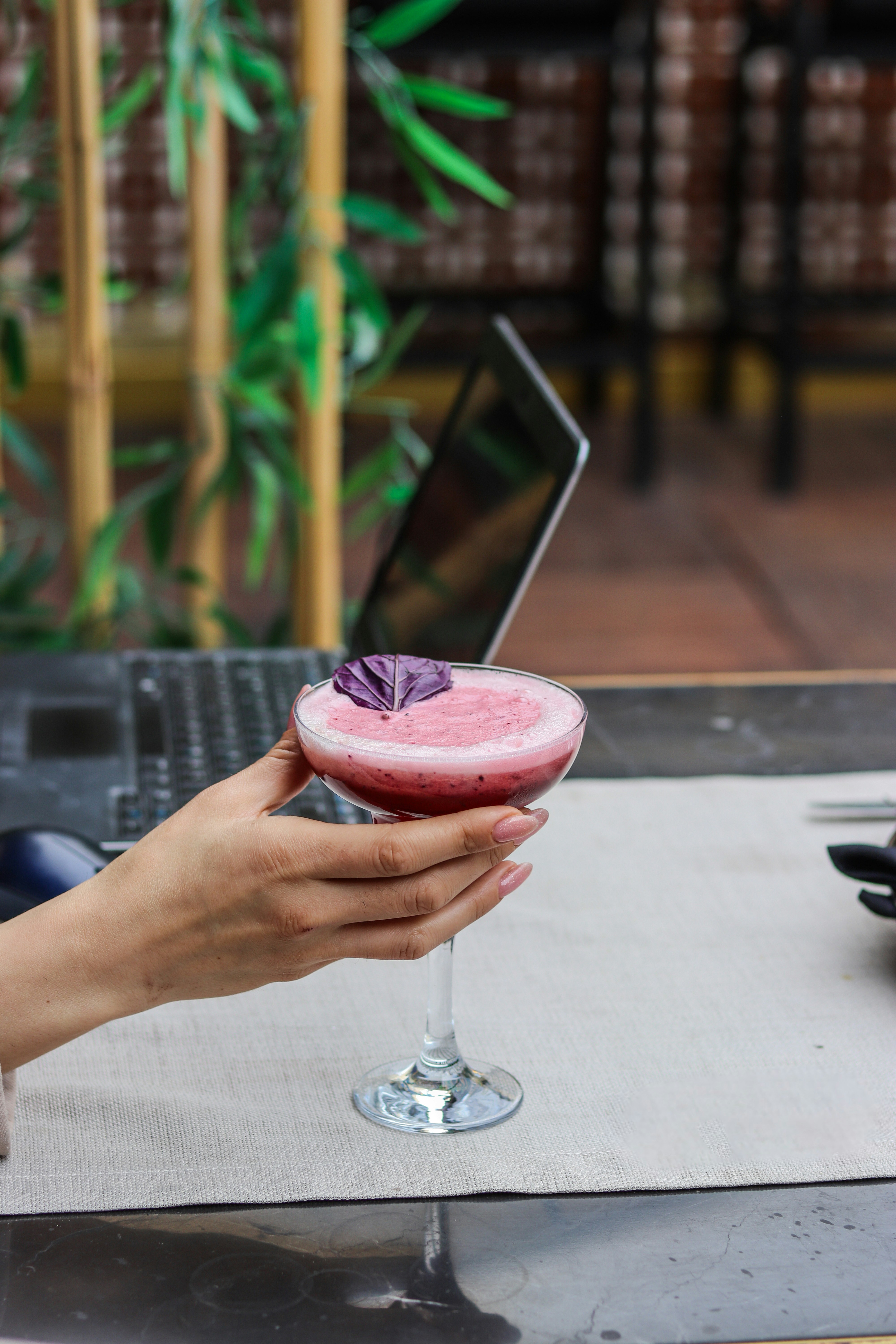 Une personne tenant une boisson rose devant un ordinateur portable
