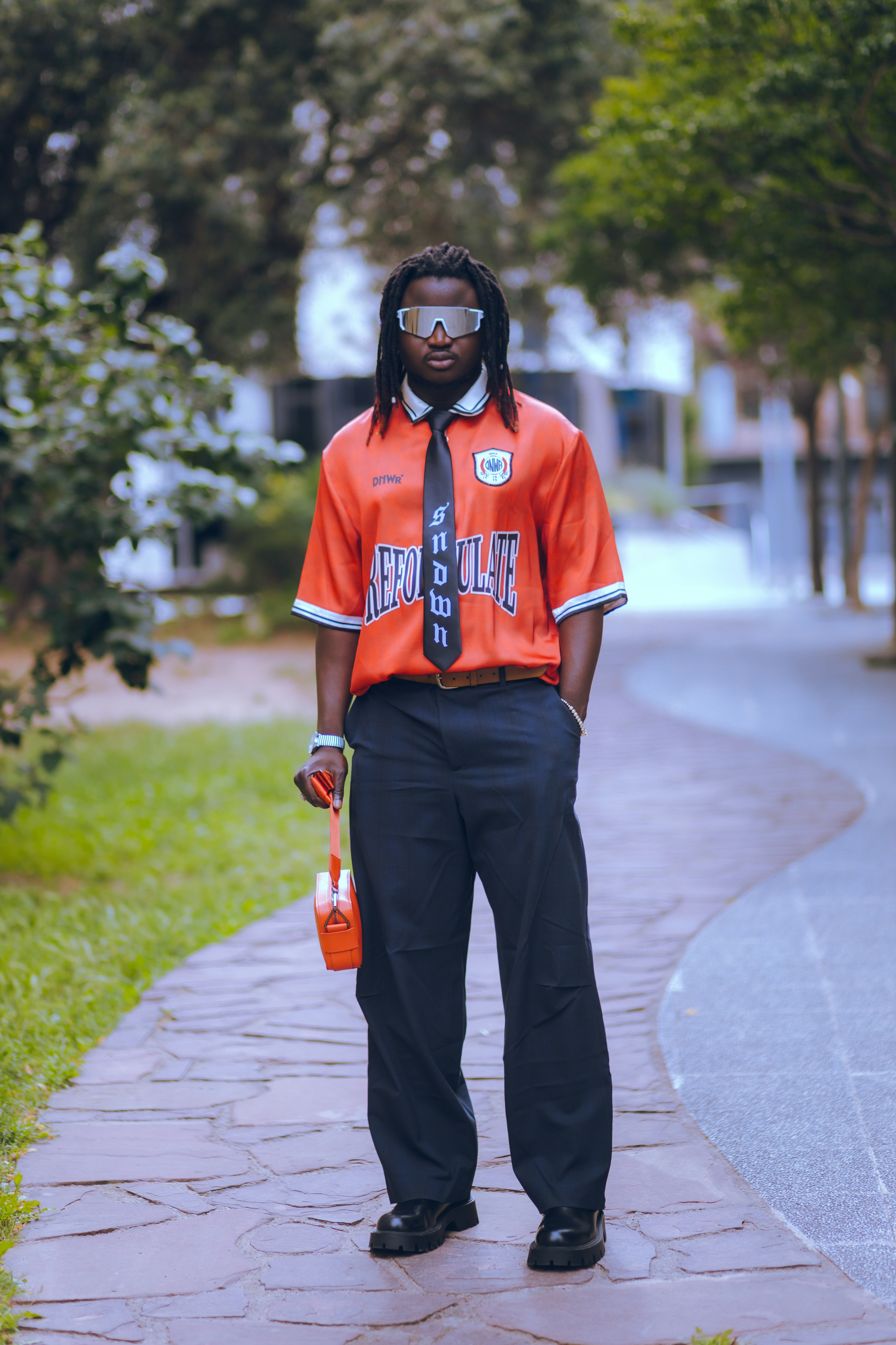A man in an orange shirt and tie standing on a sidewalk