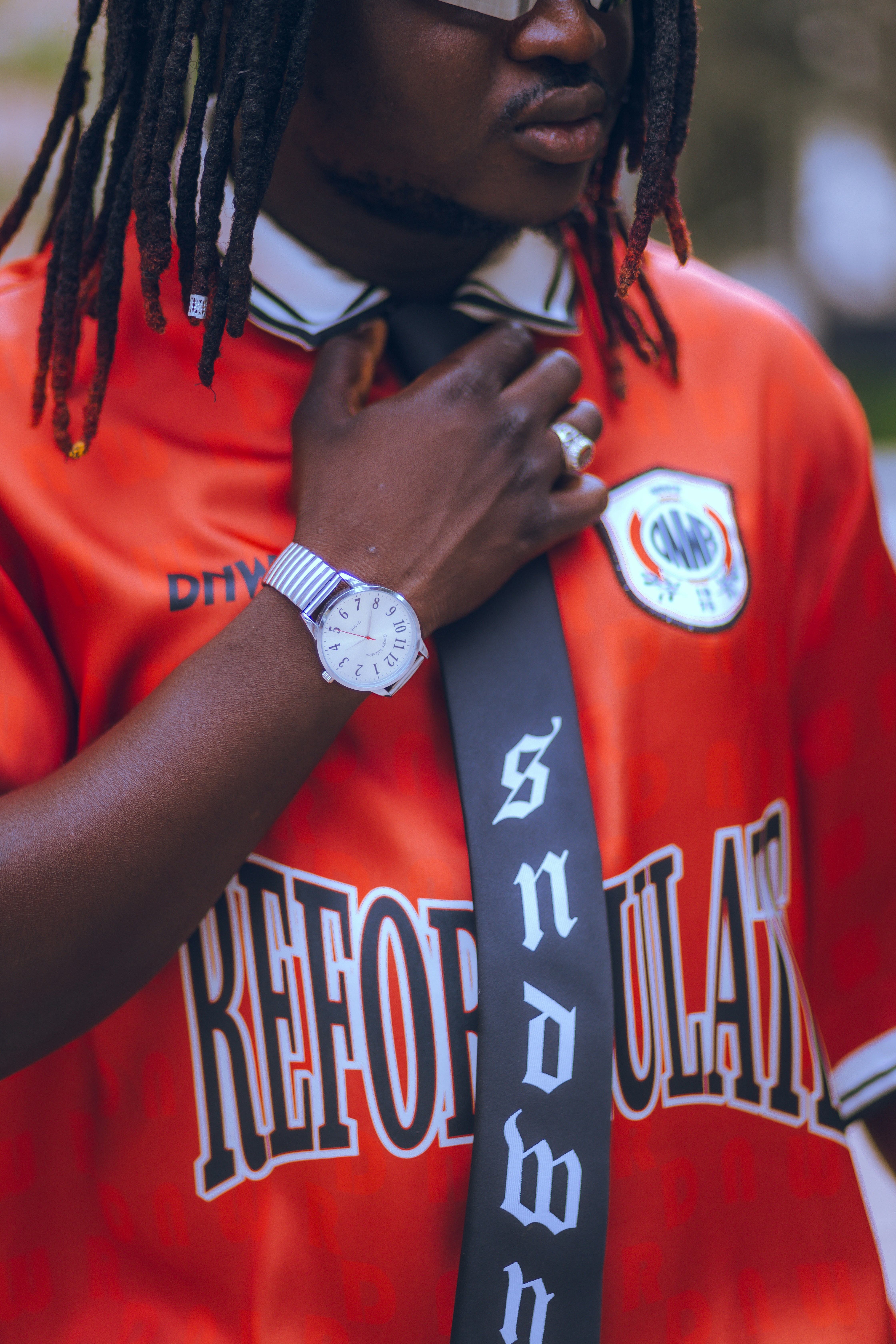 A man with dreadlocks wearing an orange shirt and tie