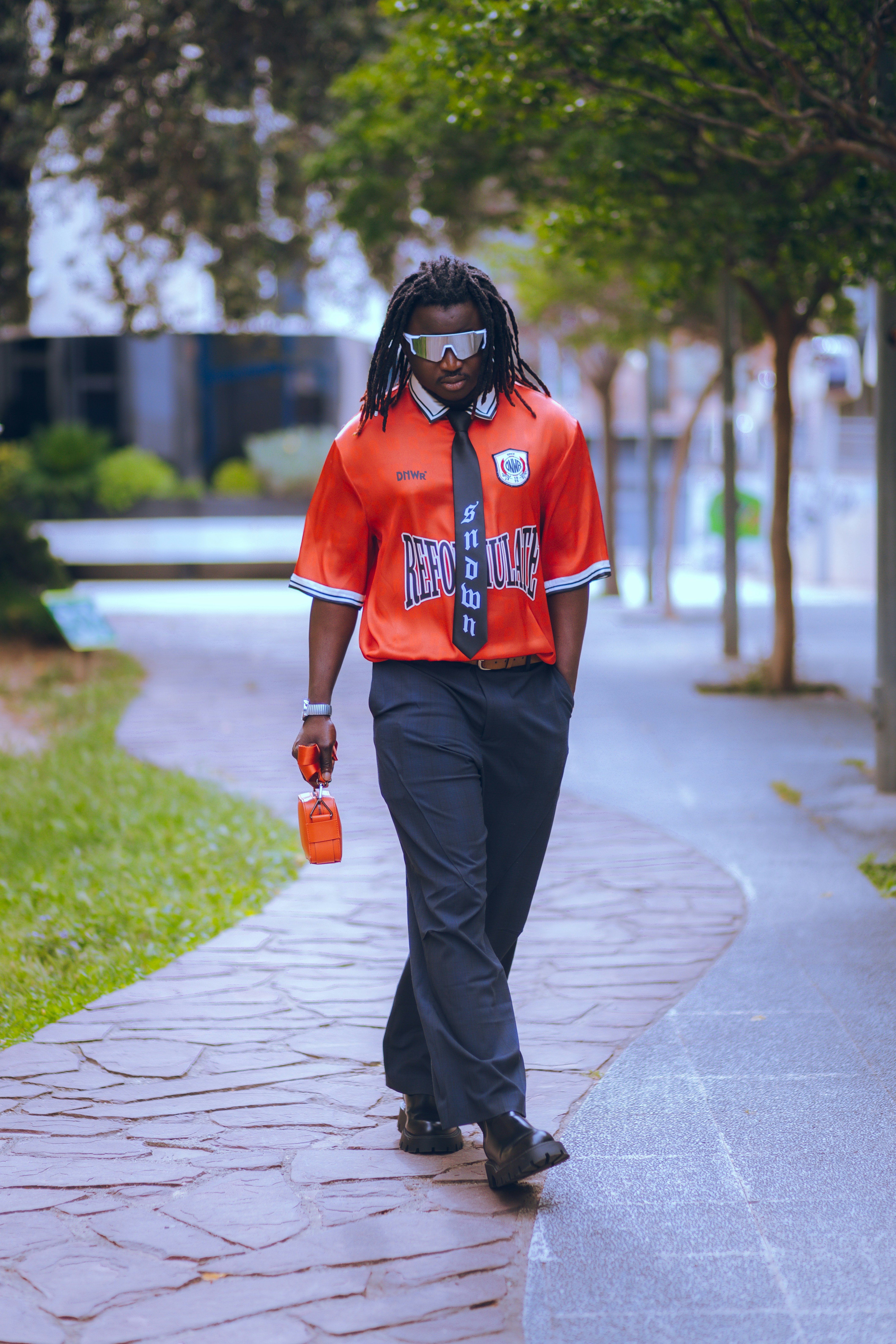 A man walking down a sidewalk wearing an orange shirt