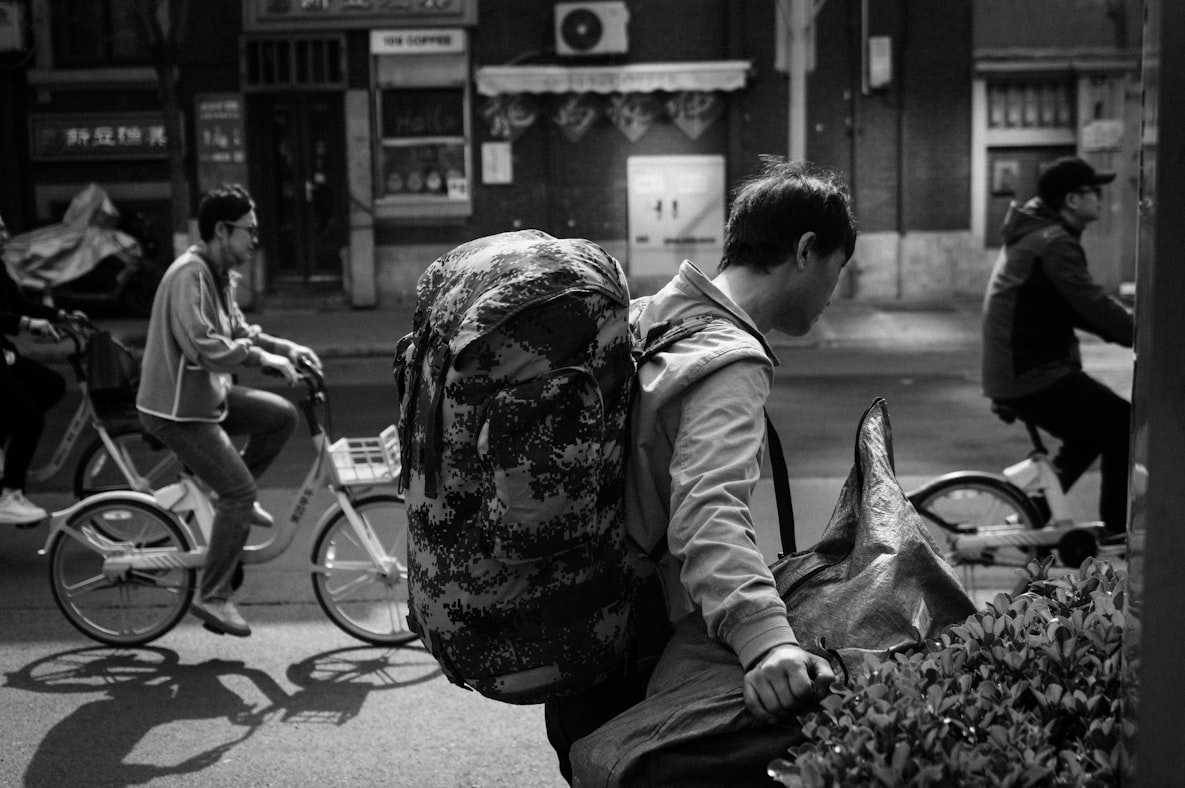 A black and white photo of a long-term traveler with a backpack at dusk, the kind who has been on the road for years