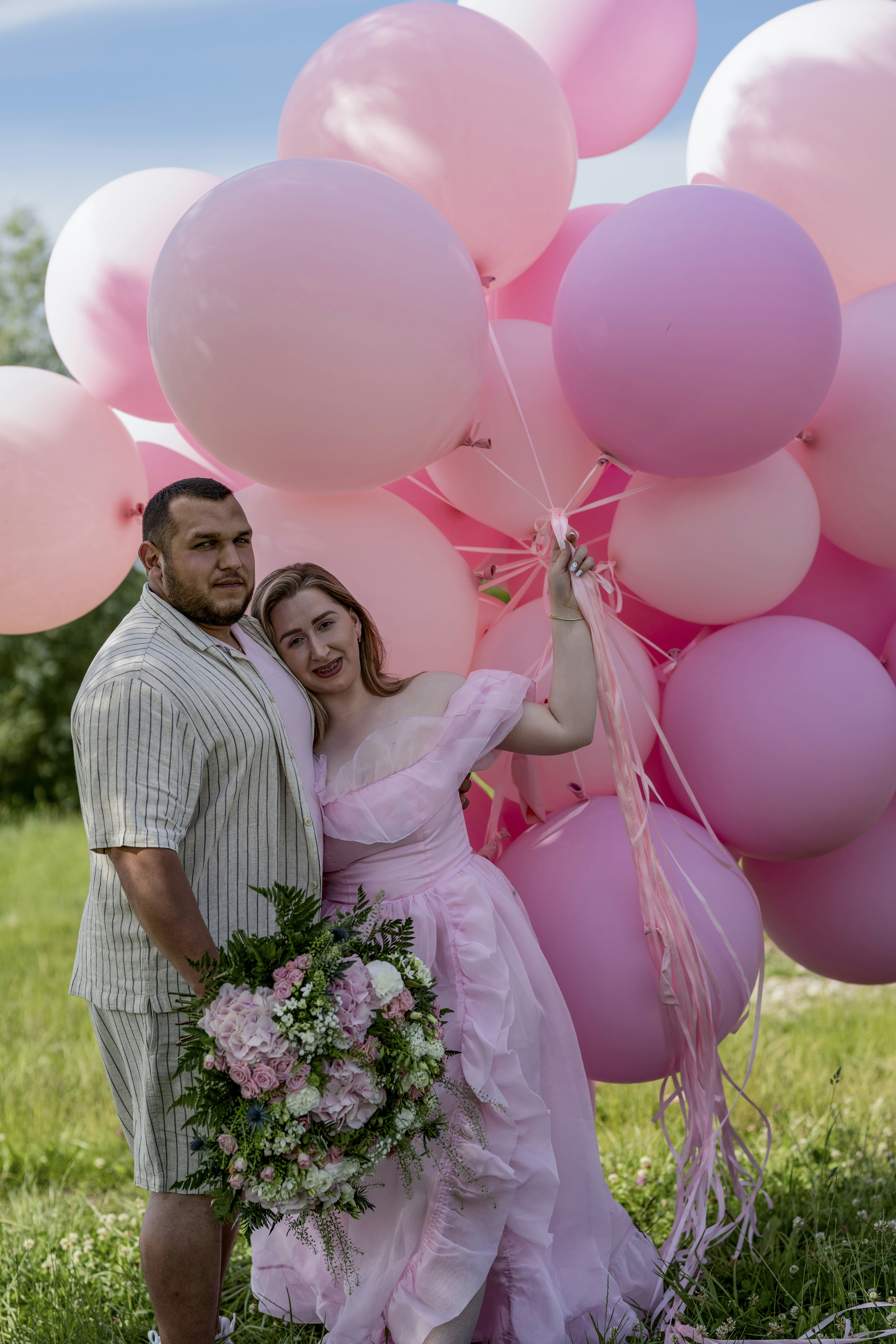 Ein Mann und eine Frau, die nebeneinander stehen und rosa Luftballons halten