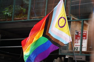 A person holding a rainbow flag in front of a building