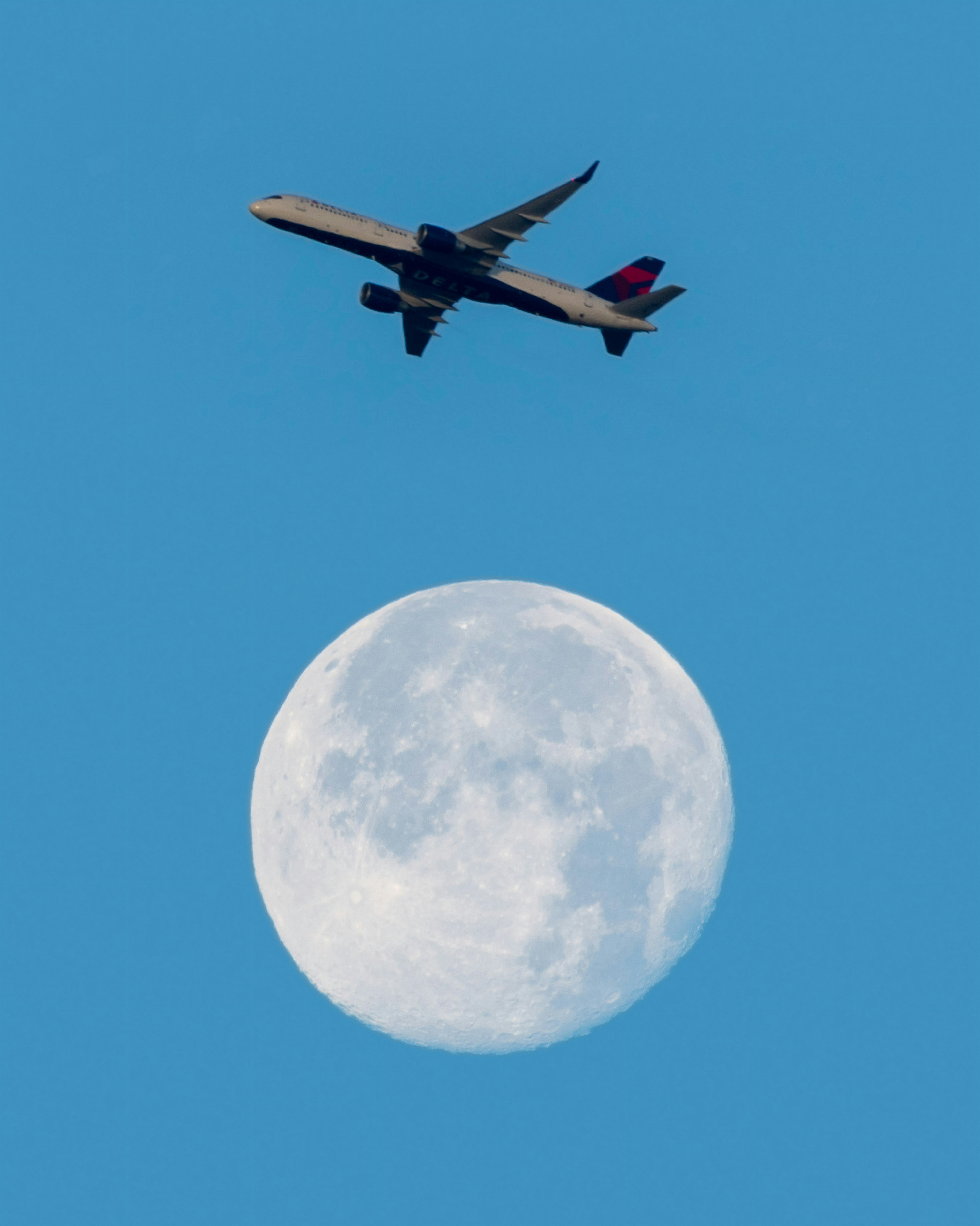 A large jetliner flying over the moon in a blue sky