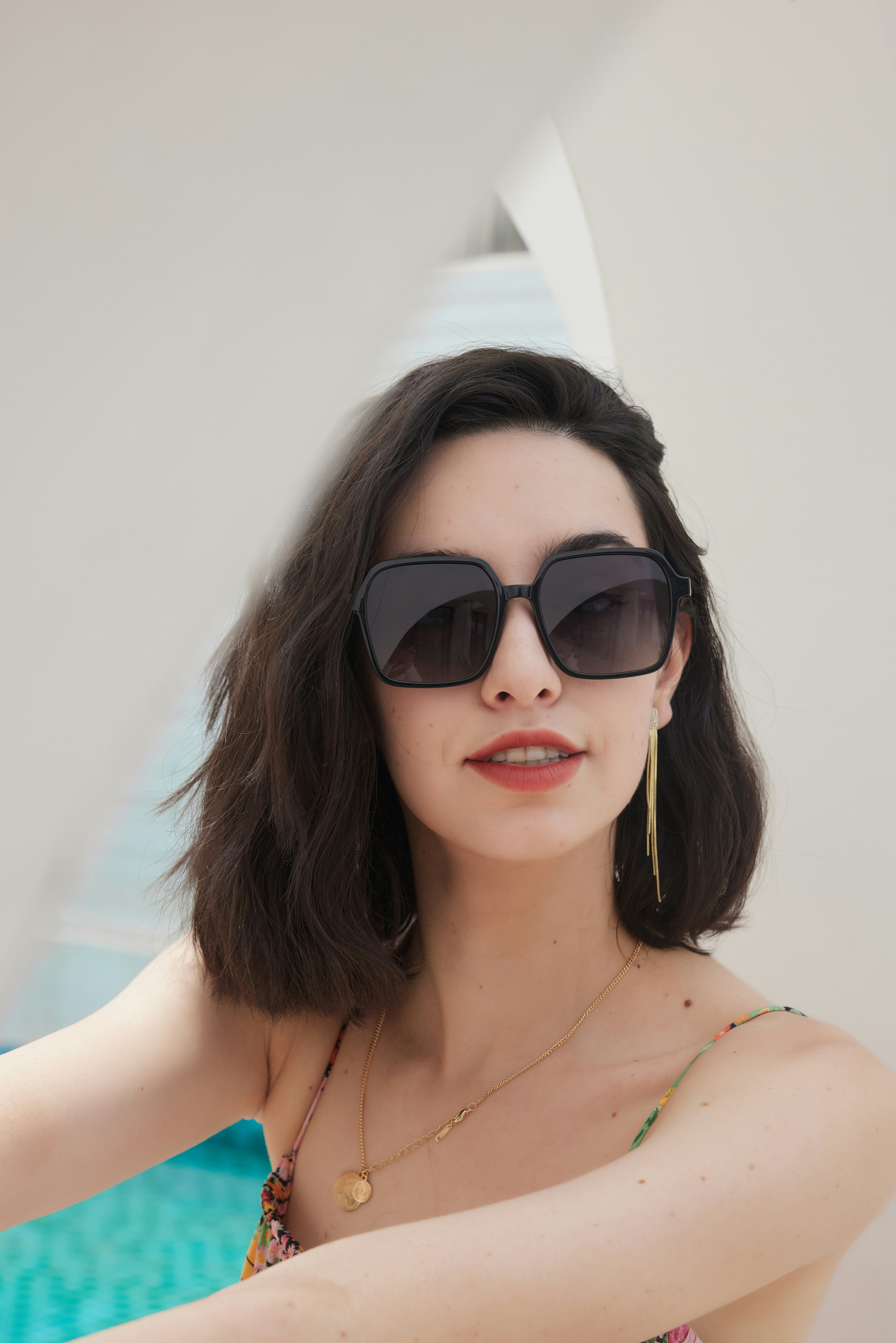 A woman in a bathing suit and sunglasses taking a selfie