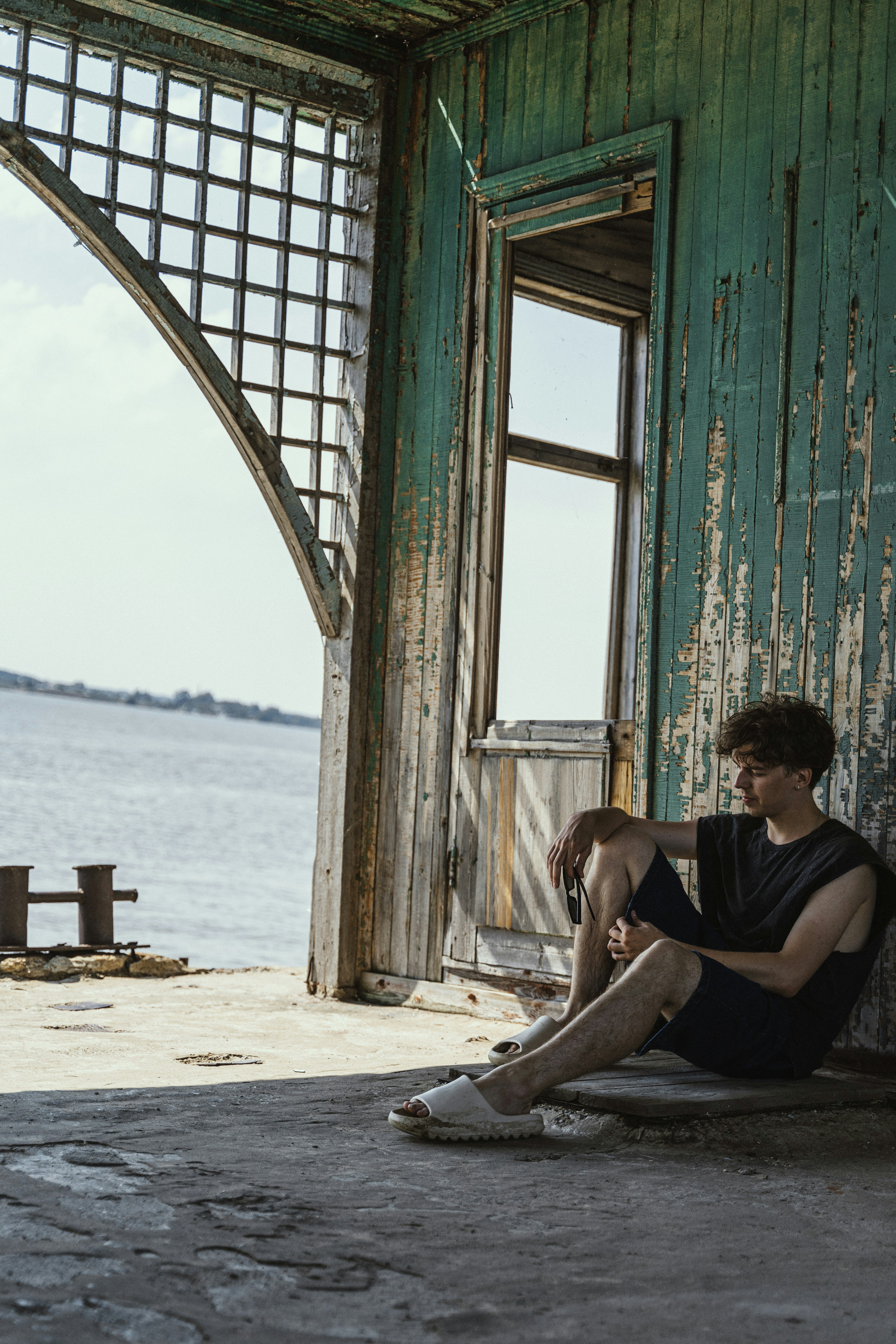 A young man sitting on the ground next to a body of water