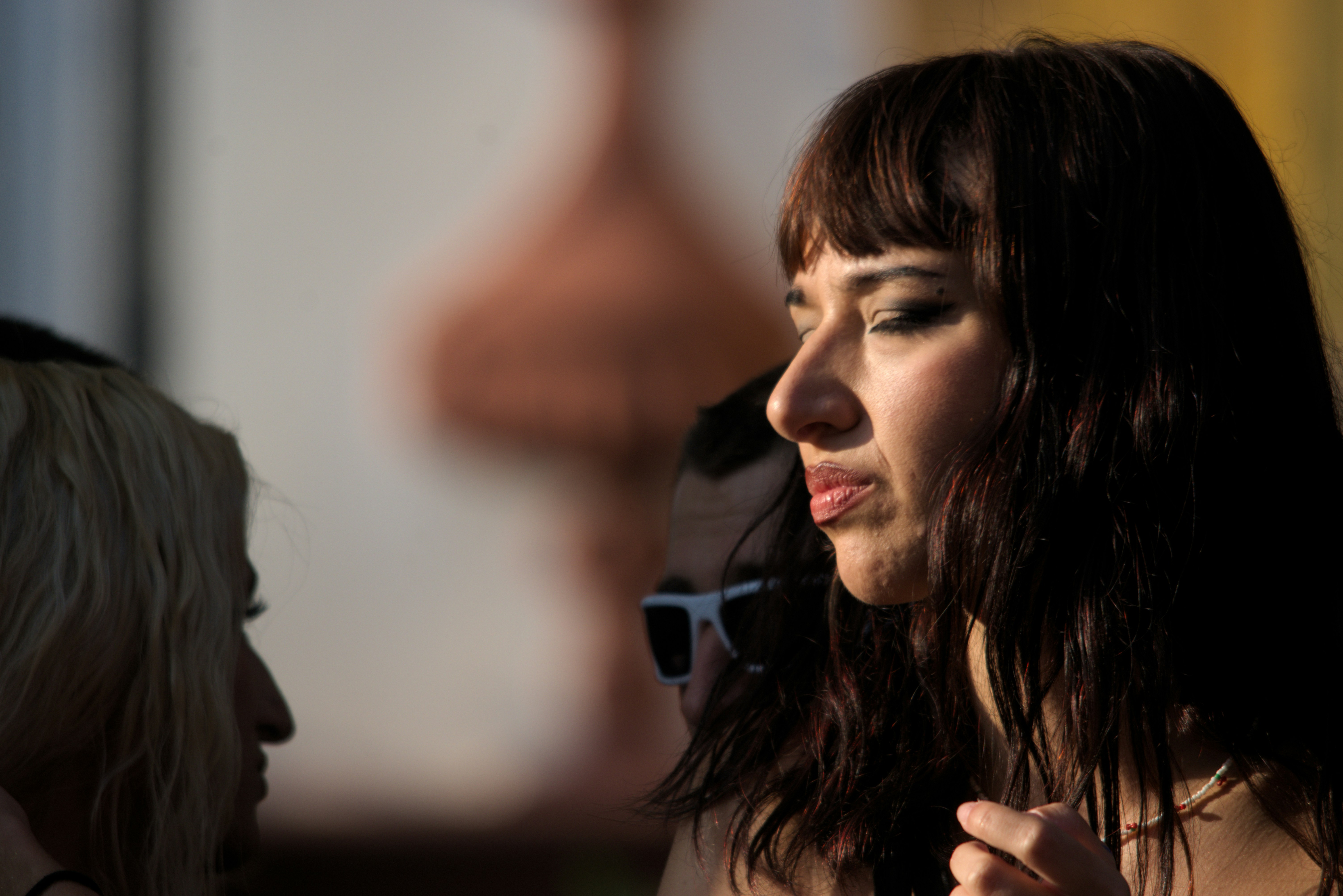 Profesionalna makeup artistkinja u elegantnom polu-profilu, crna kosa, sunčane naočare, dramatično prirodno osvetljenje