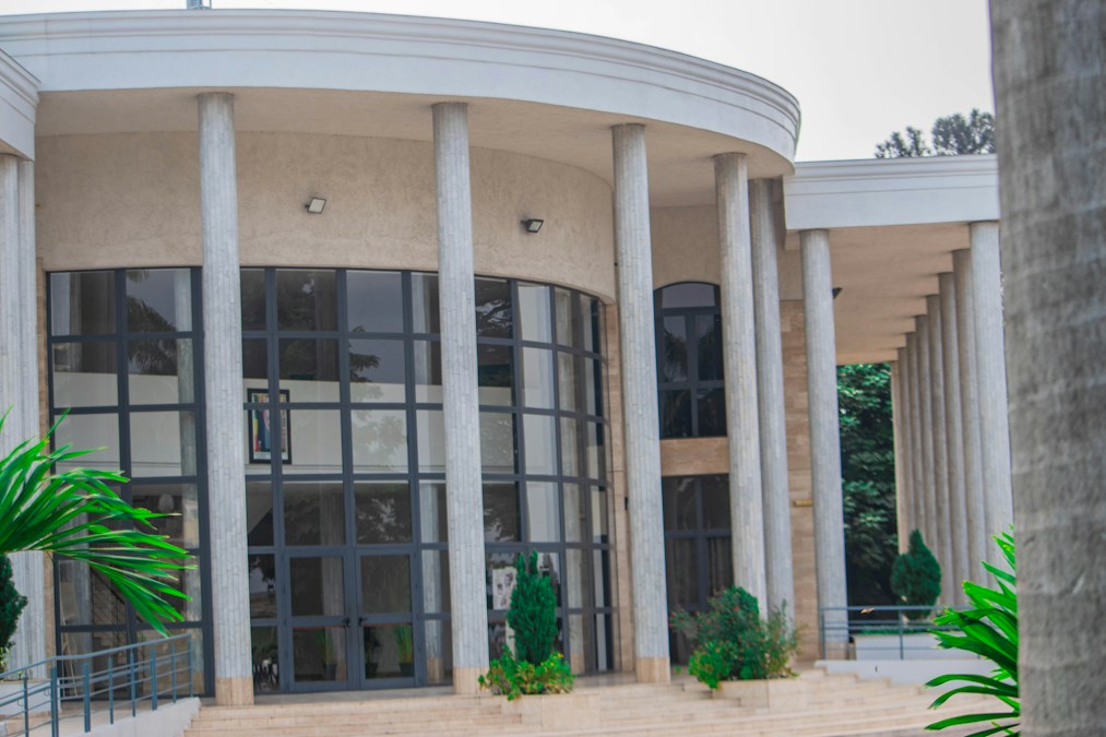 Un bâtiment circulaire à hautes colonnes blanches et grandes baies vitrées, entouré de palmiers, dans le centre de Brazzaville