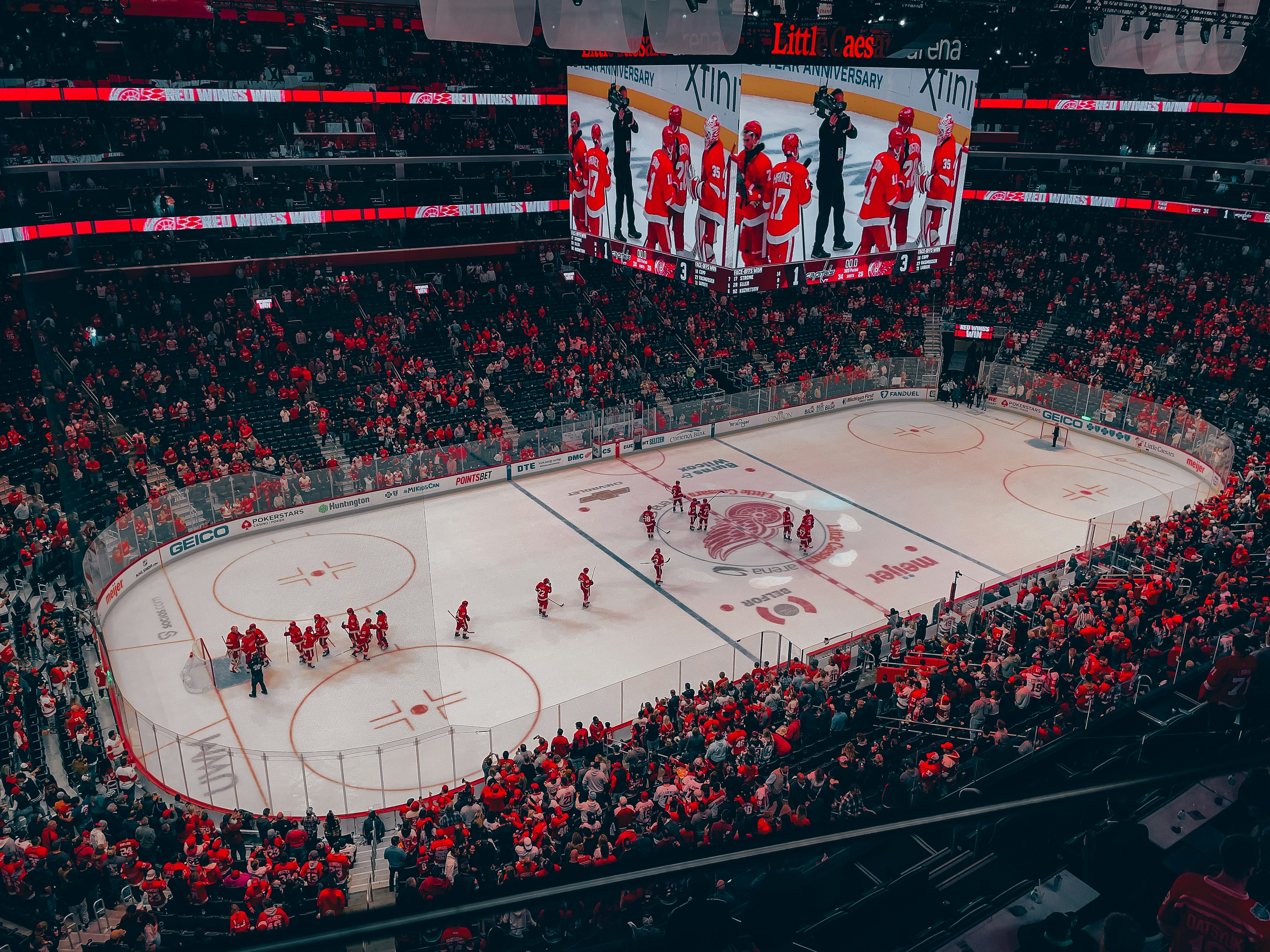 Hockey player celebrating goal on ice, orange jersey, teammates rushing over, dark arena atmosphere