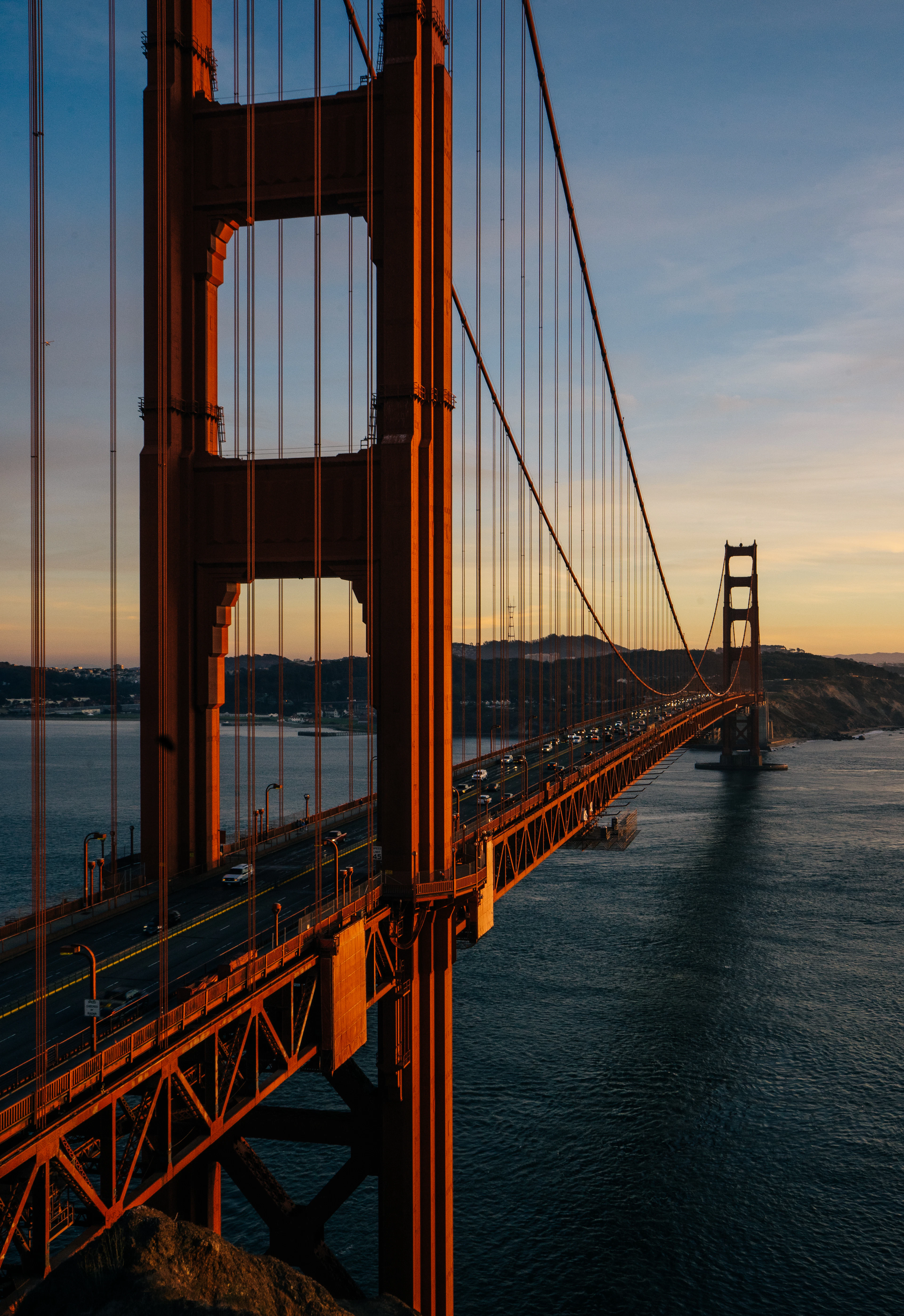 A tower of the Golden Gate Bridge close to, its cables sweeping down to the deck above the water