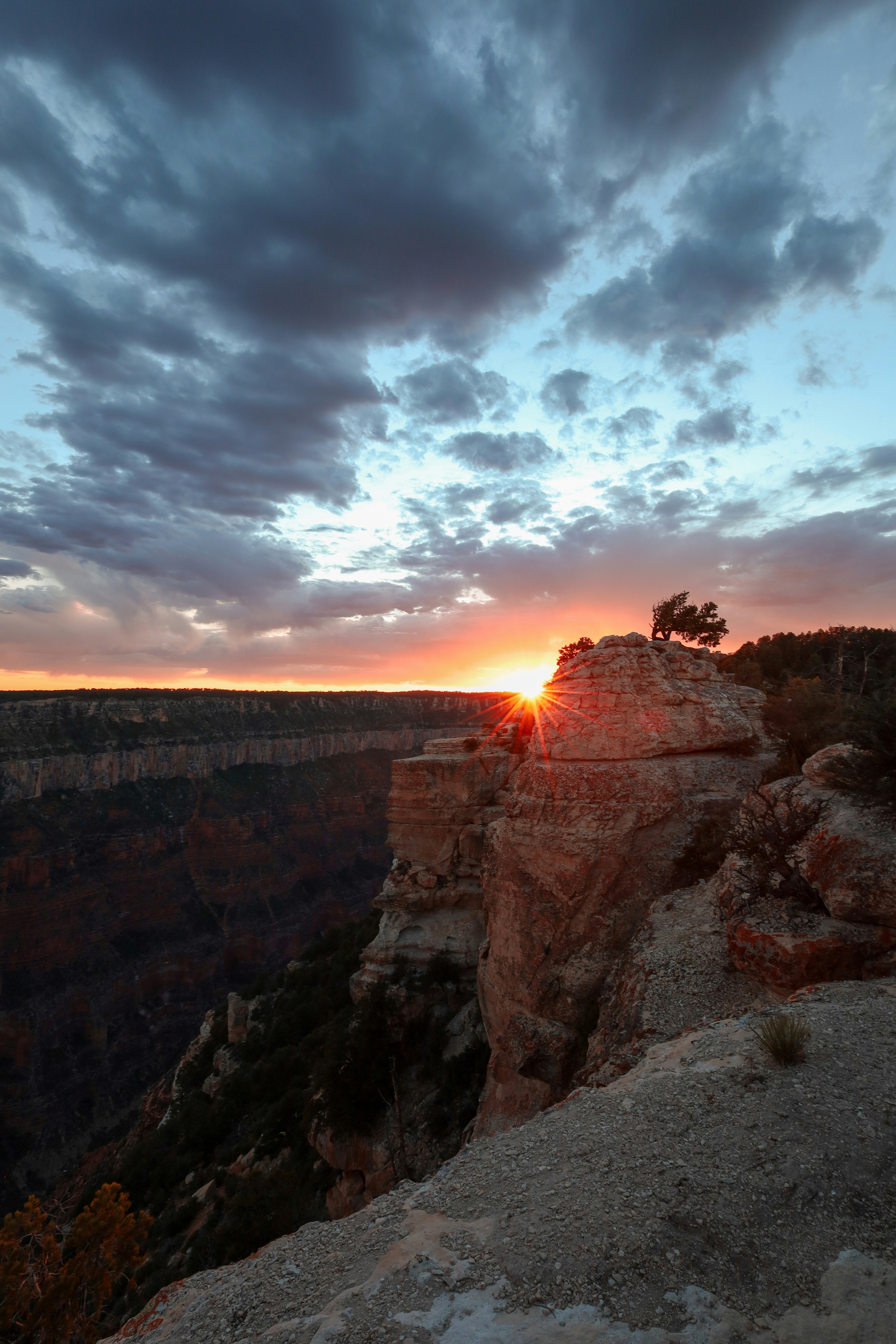 The sun is setting at the edge of a cliff